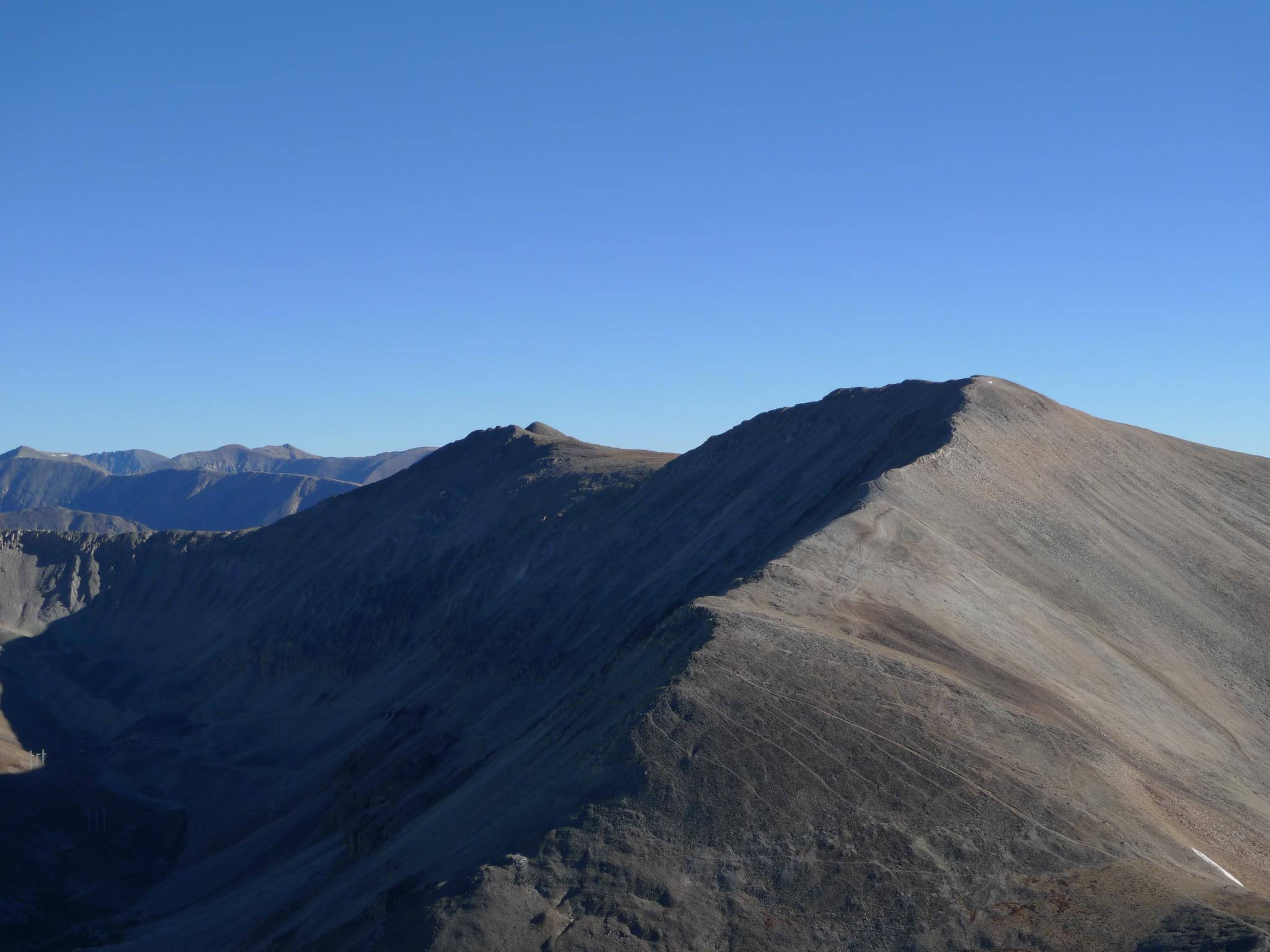 A rugged mountain ridge under a clear blue sky, with sunlit and shadowed slopes.