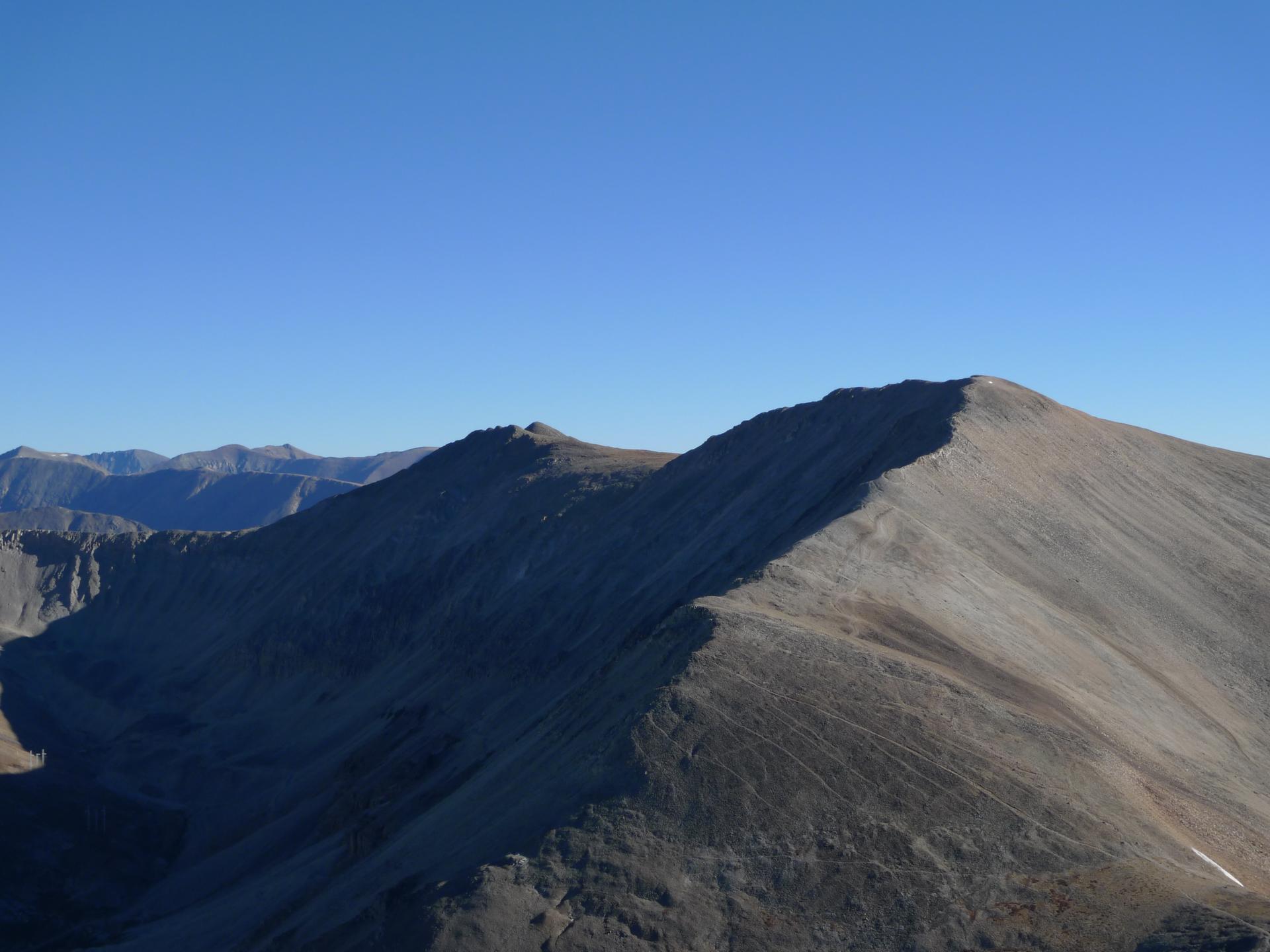 A rugged mountain ridge under a clear blue sky, with sunlit and shadowed slopes.
