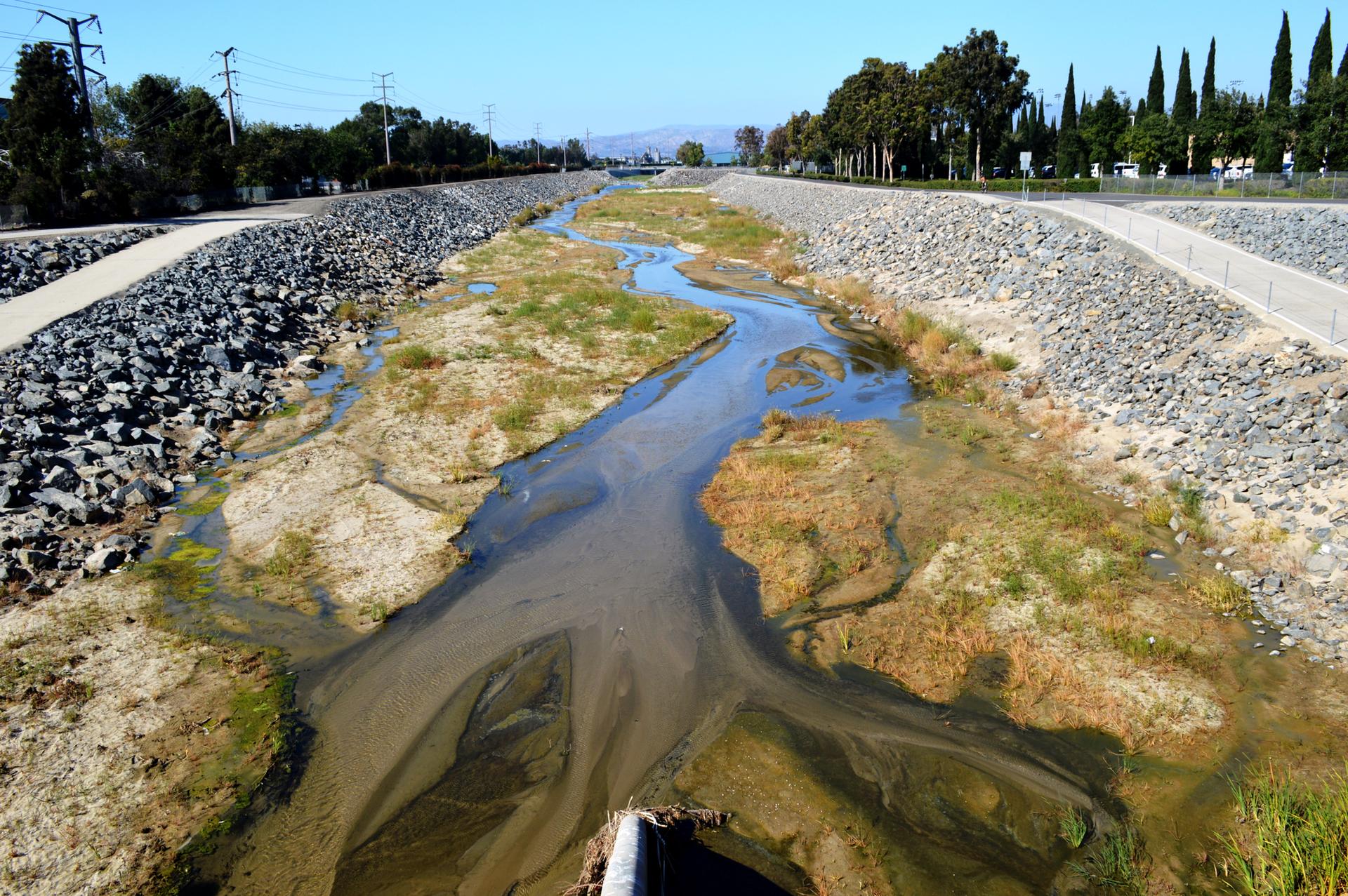 A winding, shallow river in an engineered channel under bright daylight.