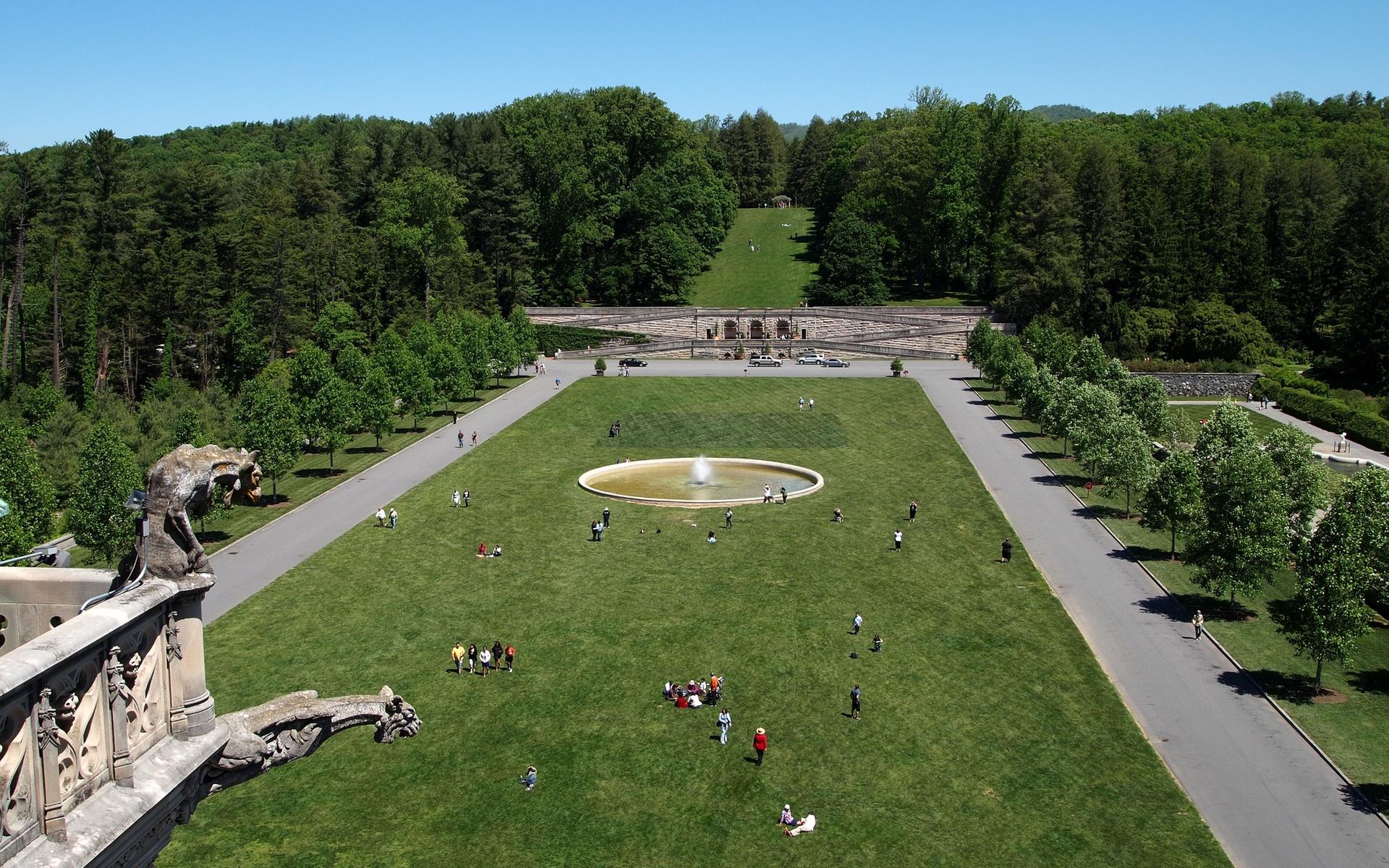 Aerial view of a vast green lawn with a circular fountain and many people.