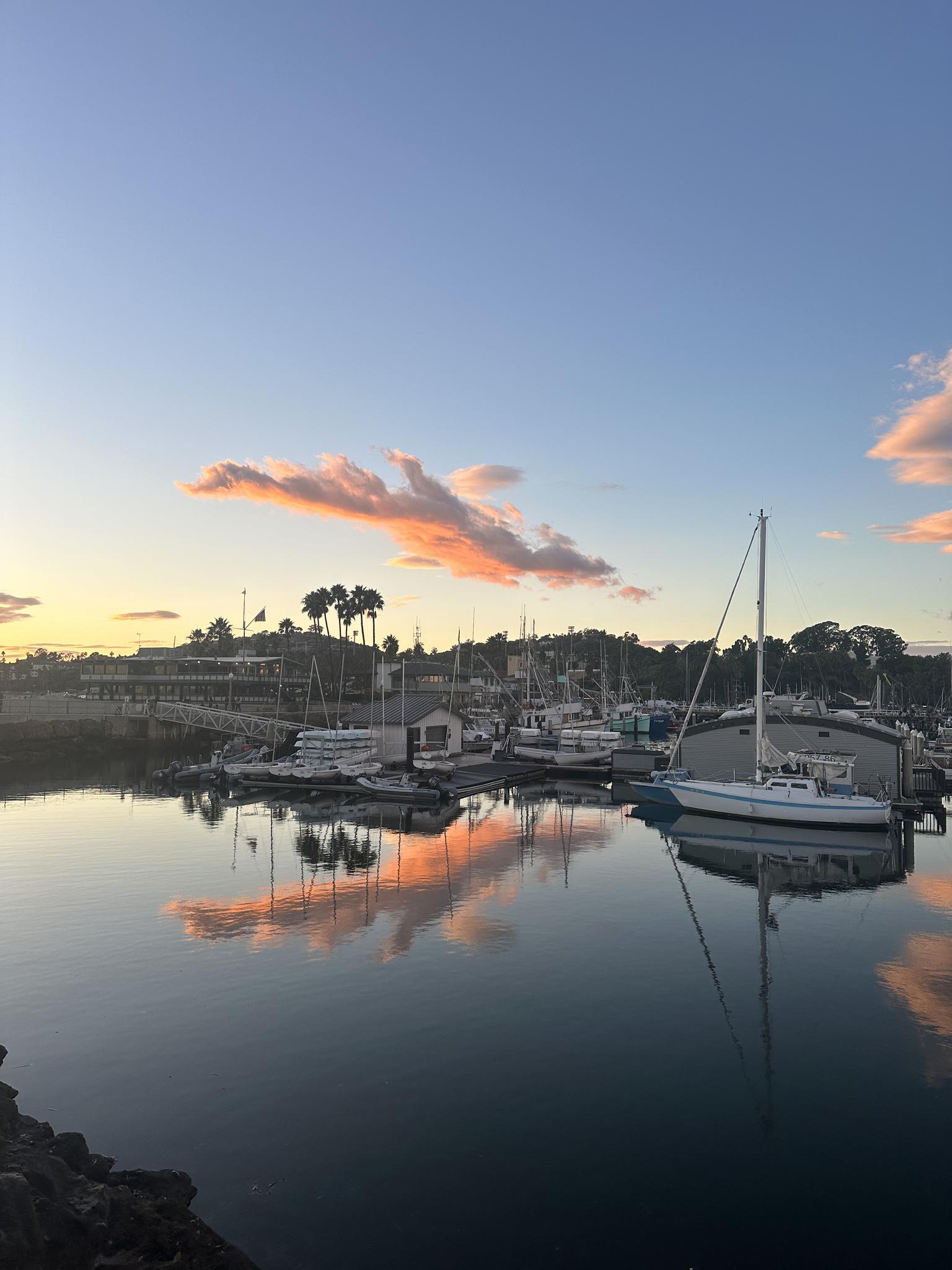 Boats docked in a marina at sunset, with colorful clouds reflecting on water.