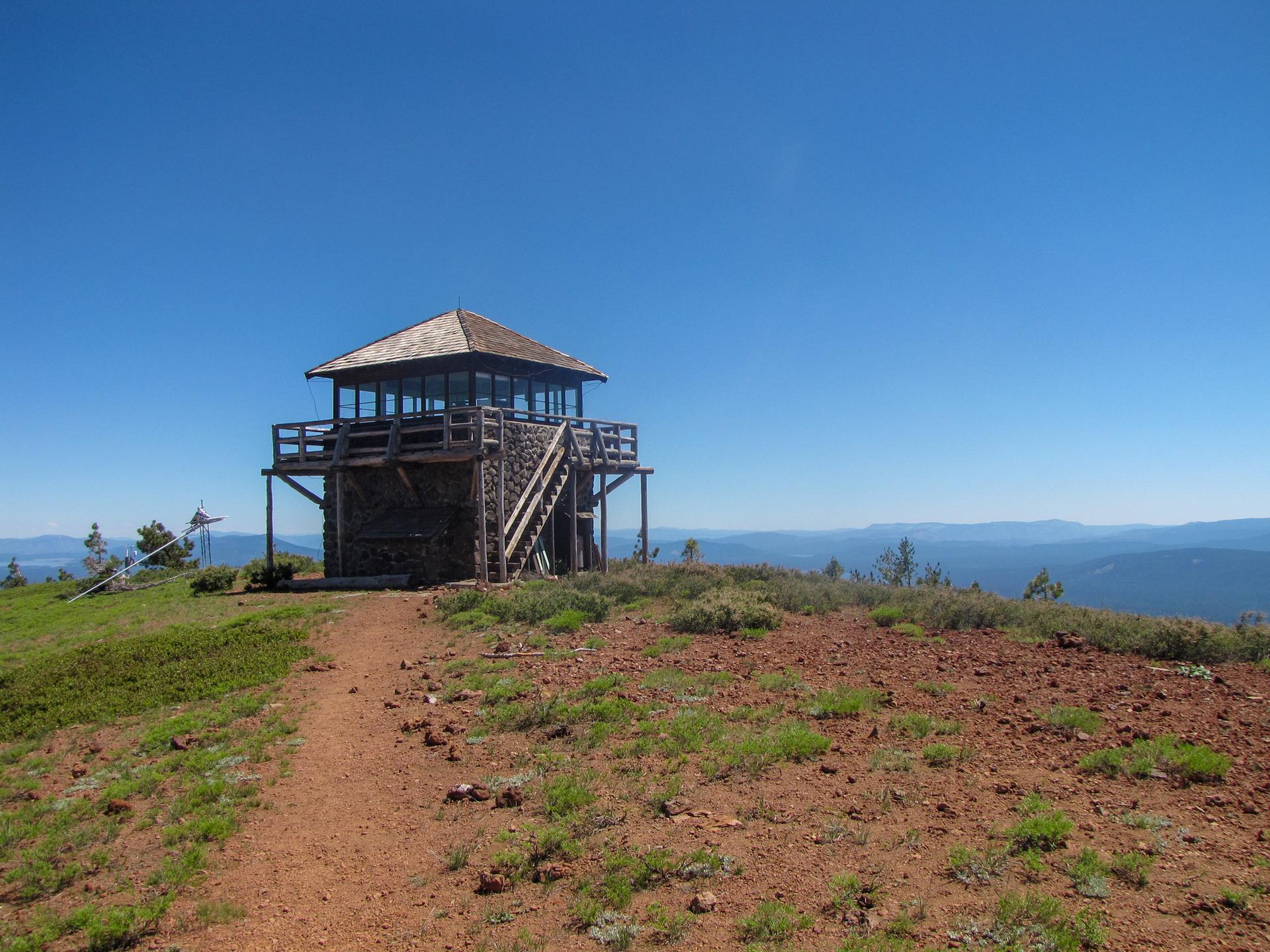 A wooden fire lookout tower on a dry hilltop under a clear blue sky.