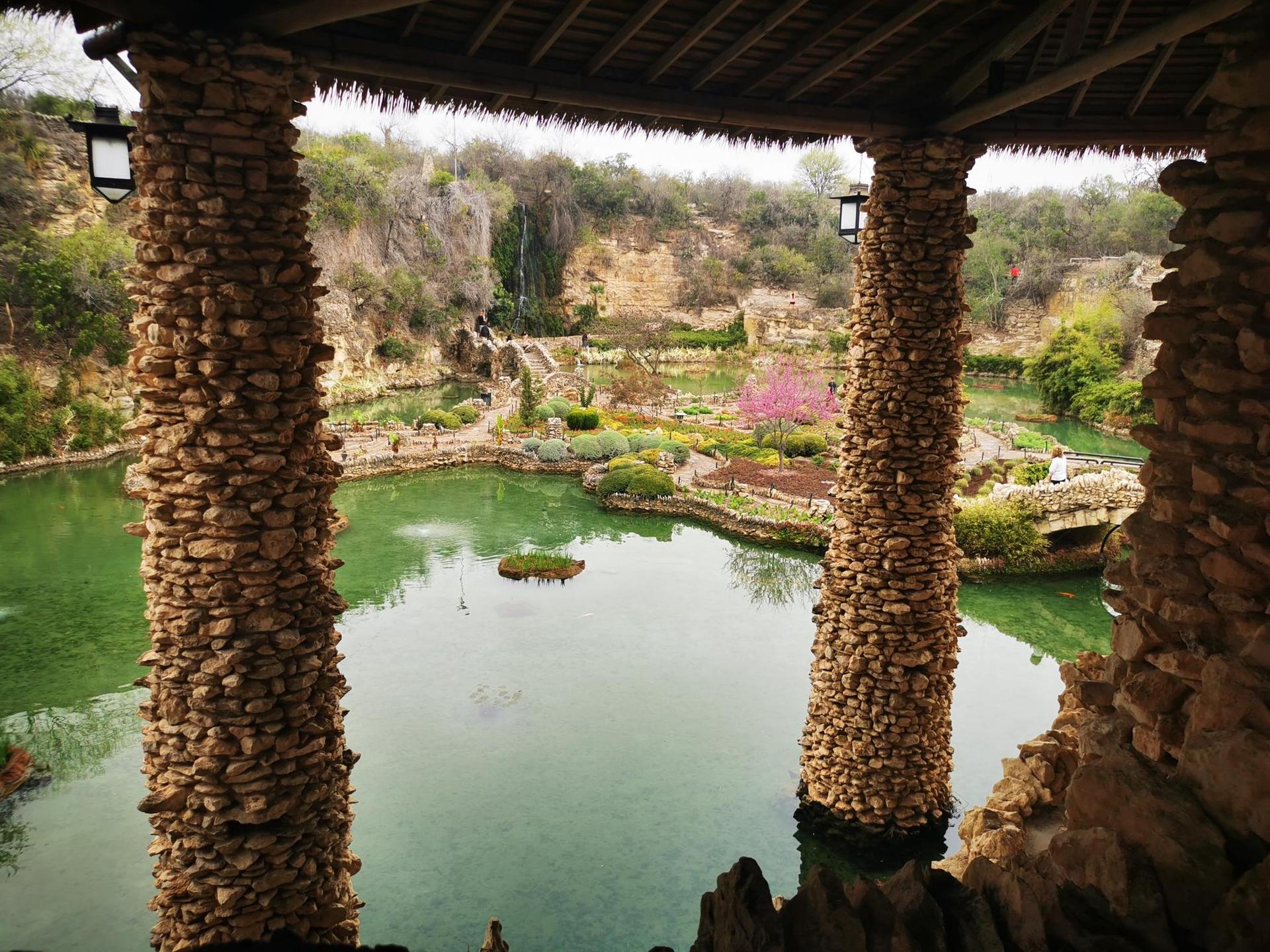 View of a lush garden with green ponds through stone pillars.