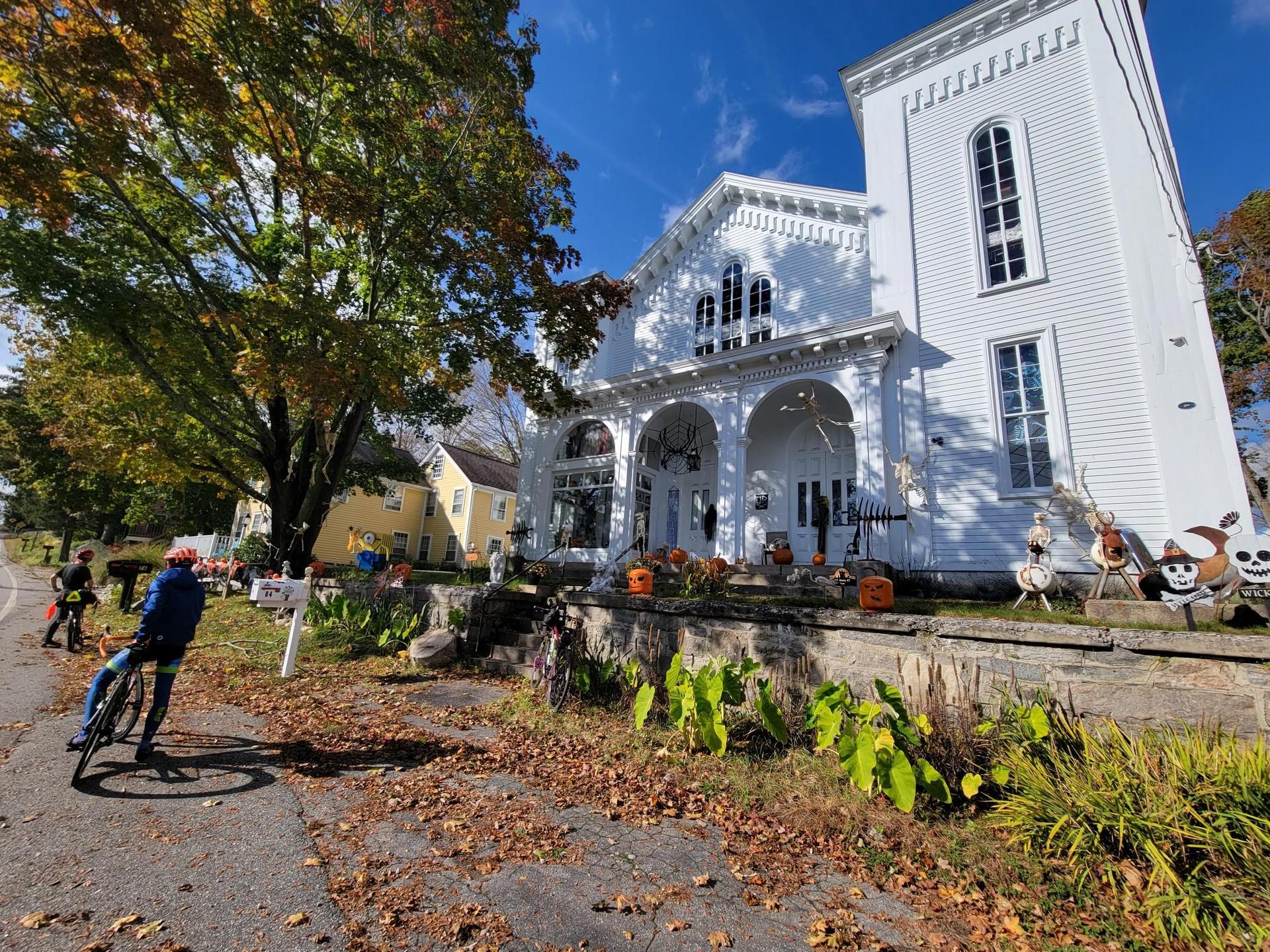 A person on a bicycle near a large white building with autumn decorations.