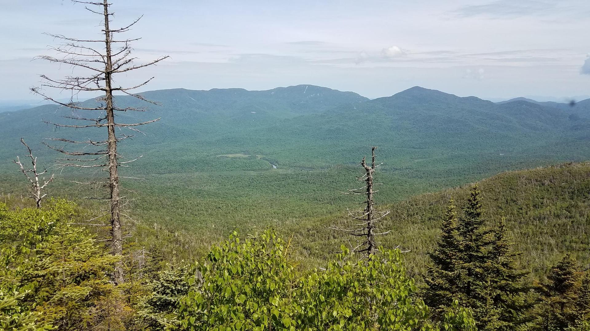 Expansive view of rolling green mountains under a bright, cloudy sky.