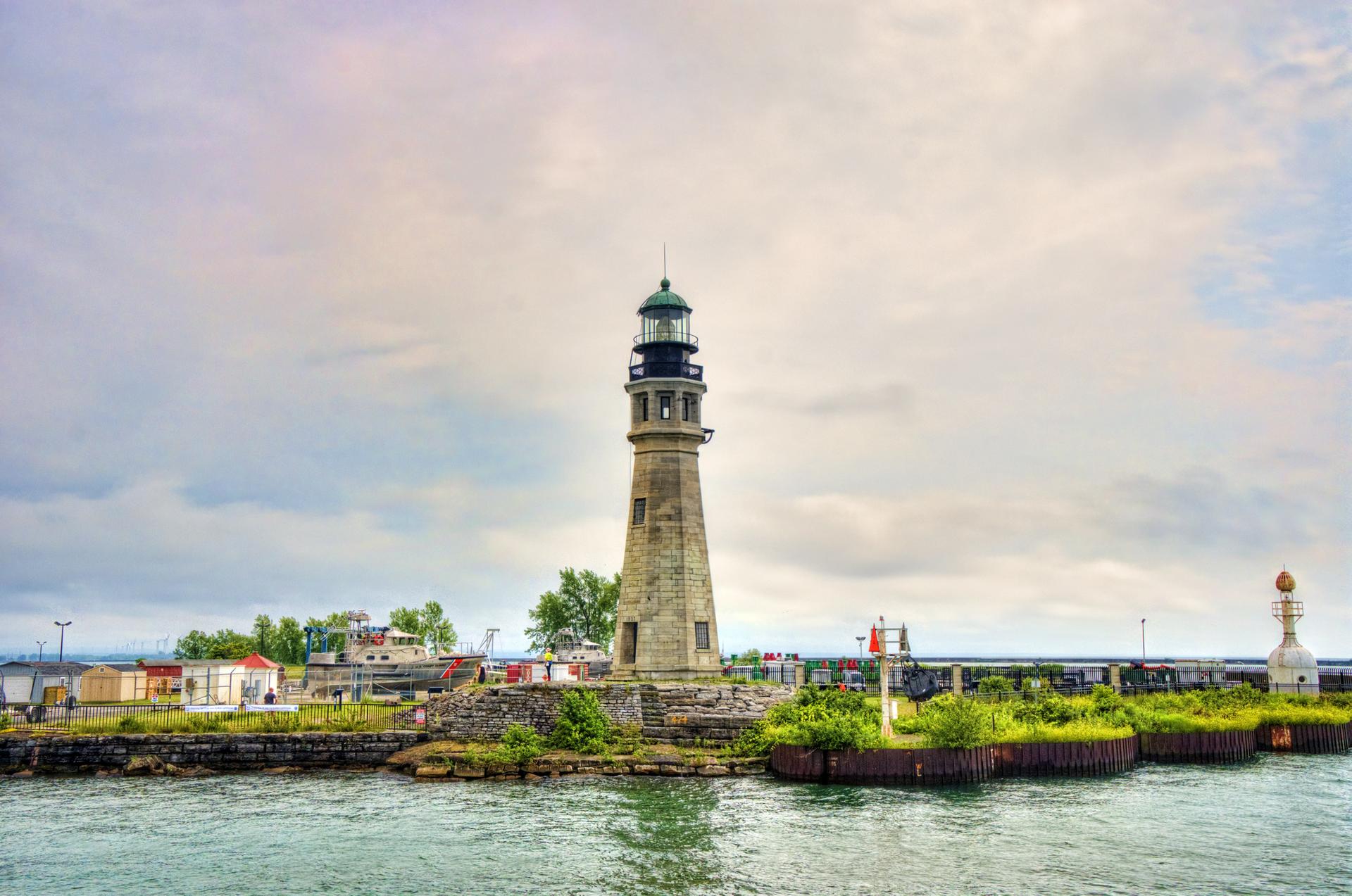 A tall stone lighthouse with a green top stands by water under a cloudy sky.