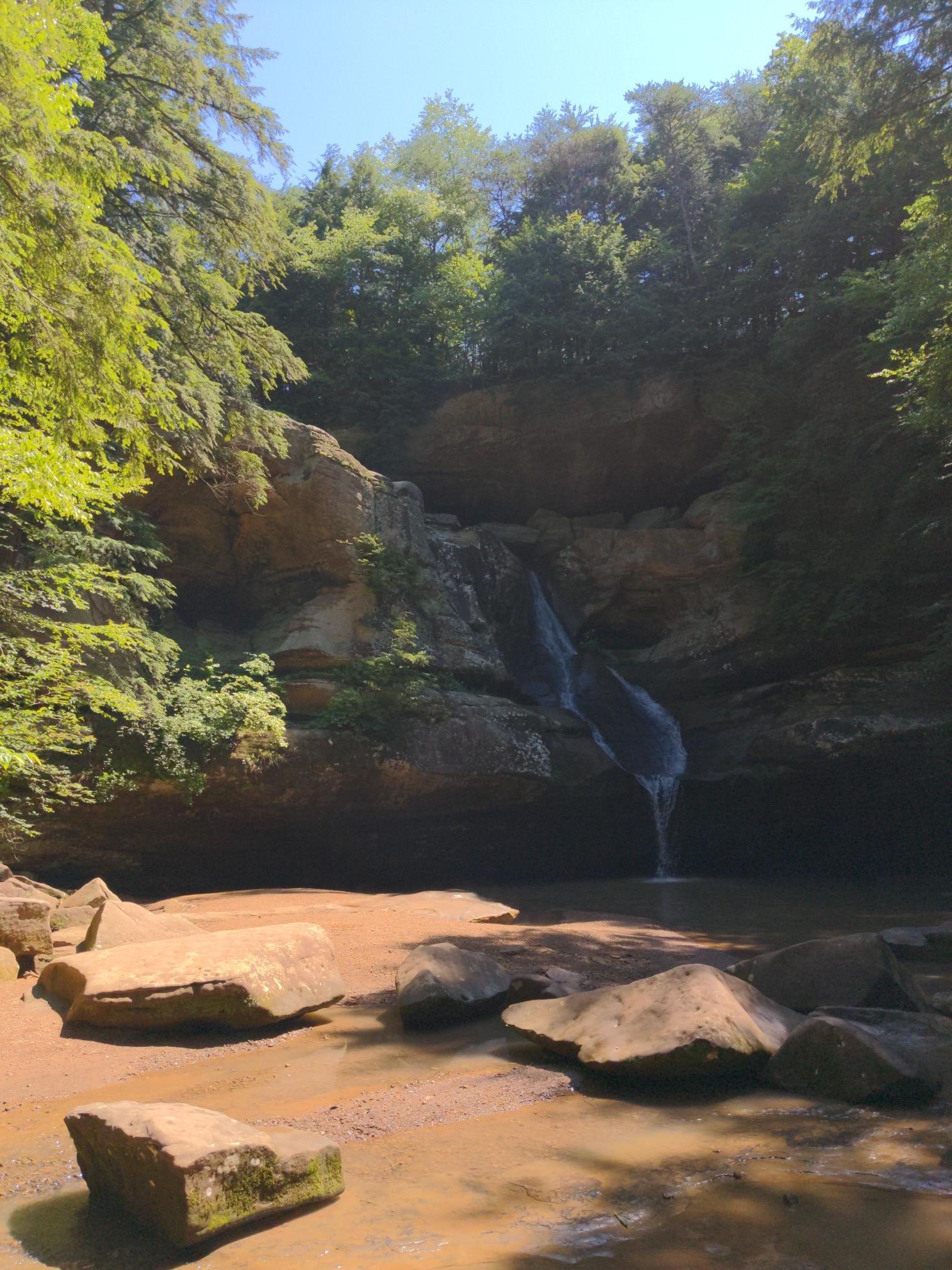 Waterfall cascades into a shallow pool in a sunny, rocky gorge.