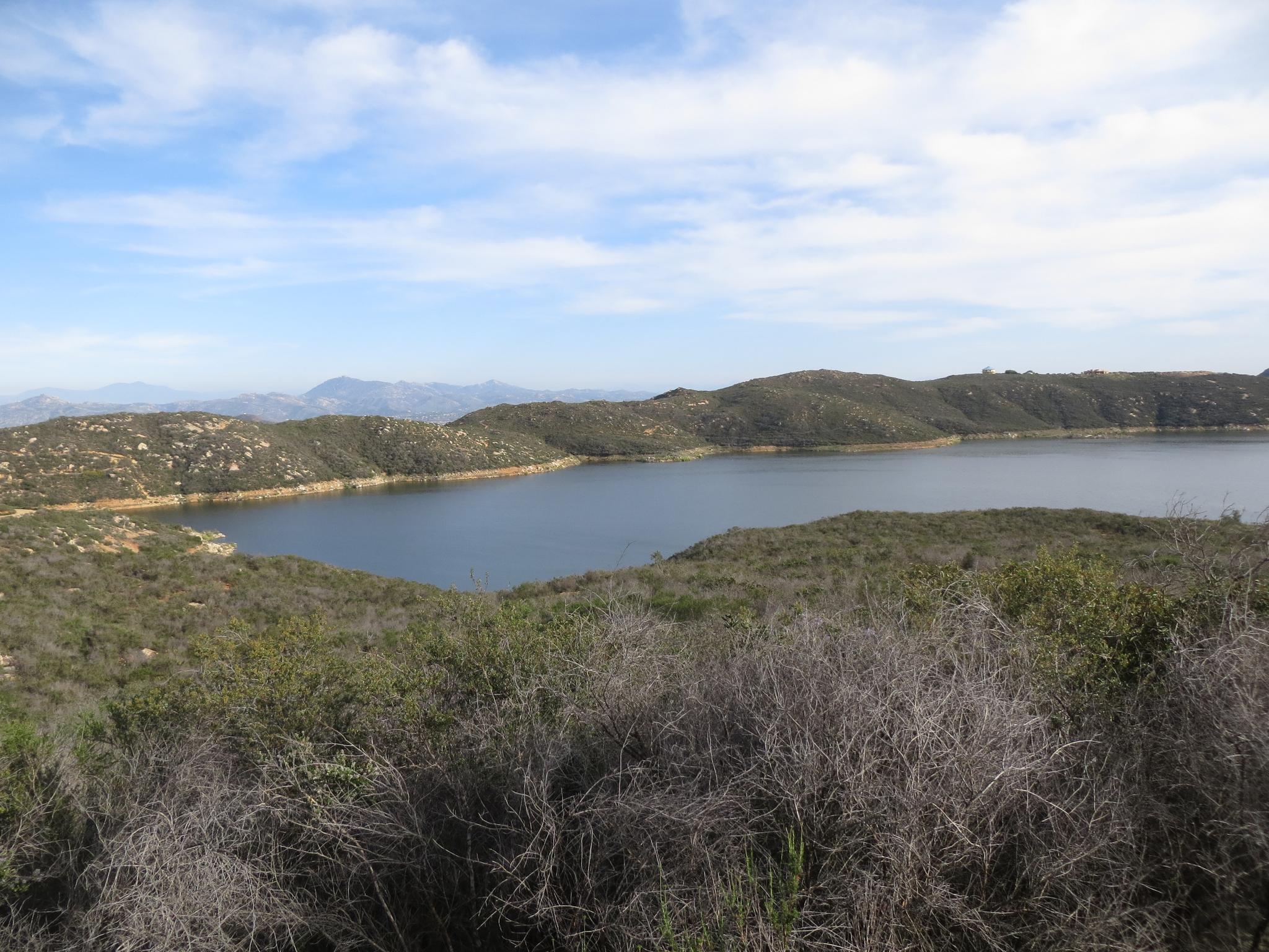 A wide lake nestled among scrub-covered hills under a partly cloudy sky.