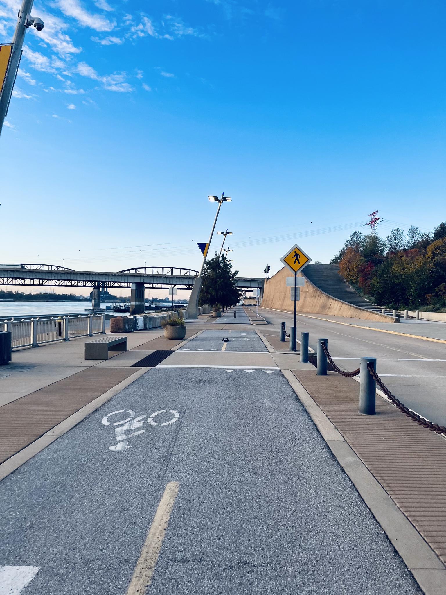 A paved path with a bicycle symbol next to a road and distant bridge.