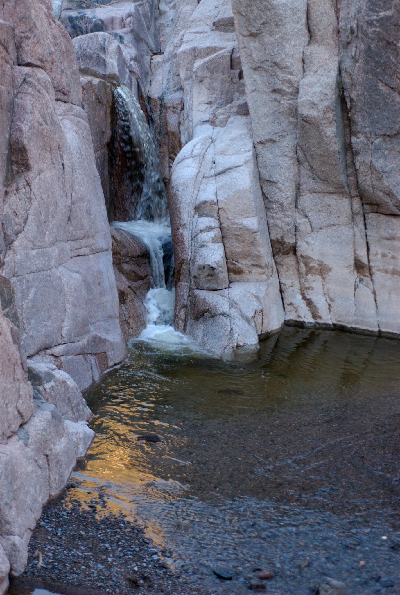 Waterfall cascades into a dark pool within a narrow, rocky canyon.