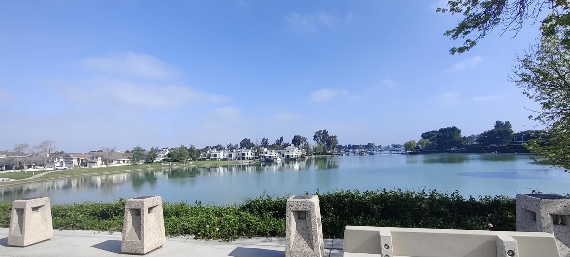 Panoramic view of a calm lake with distant buildings under blue sky.
