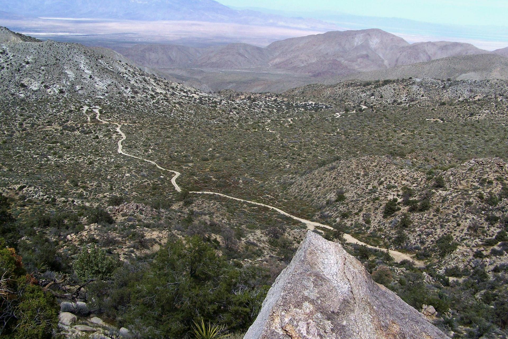 Overhead view of a winding dirt path through a vast, arid valley.
