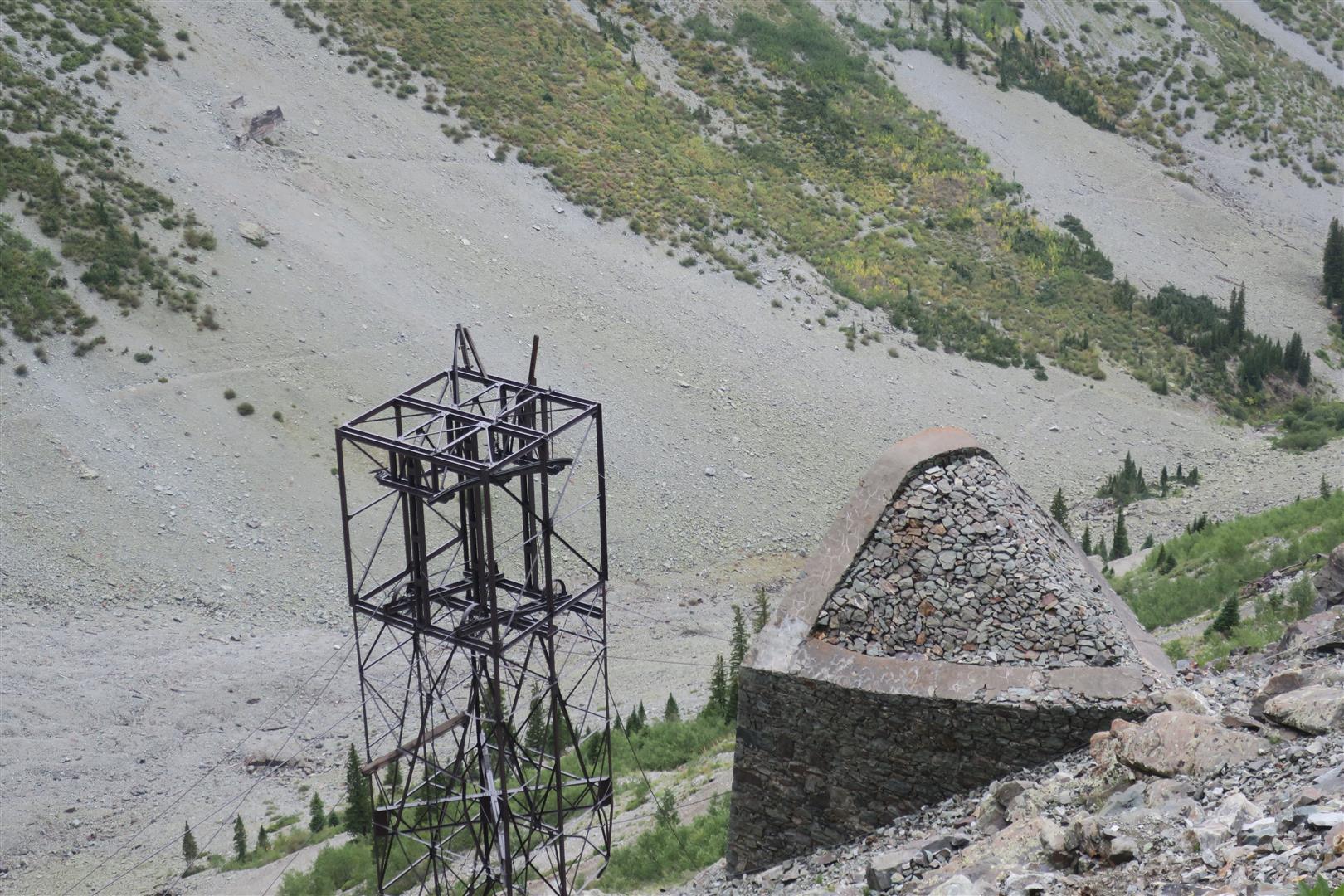 Metal structure and stone mound on a steep, rocky mountain slope.