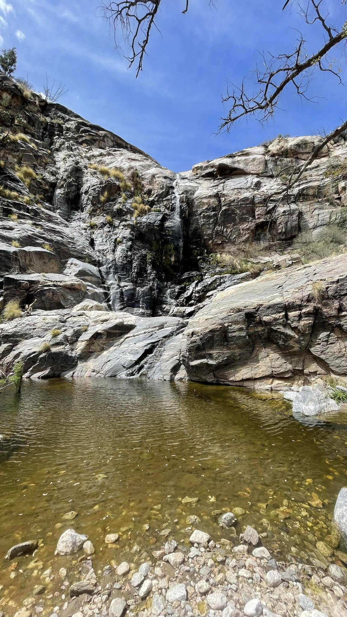 Waterfall cascading into a clear pool surrounded by rocky cliffs.