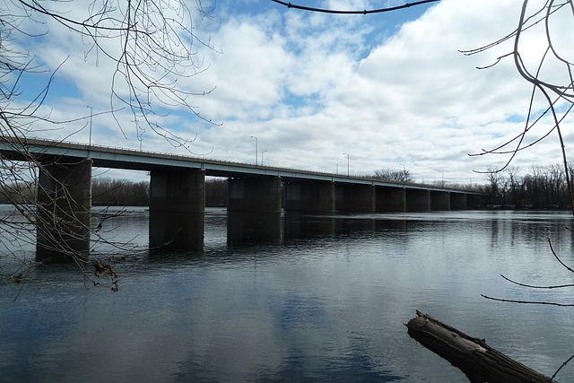 Long bridge with concrete piers spanning a wide river under a cloudy sky.