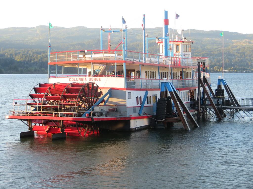 Large red and white paddlewheel boat docked on water at golden hour.