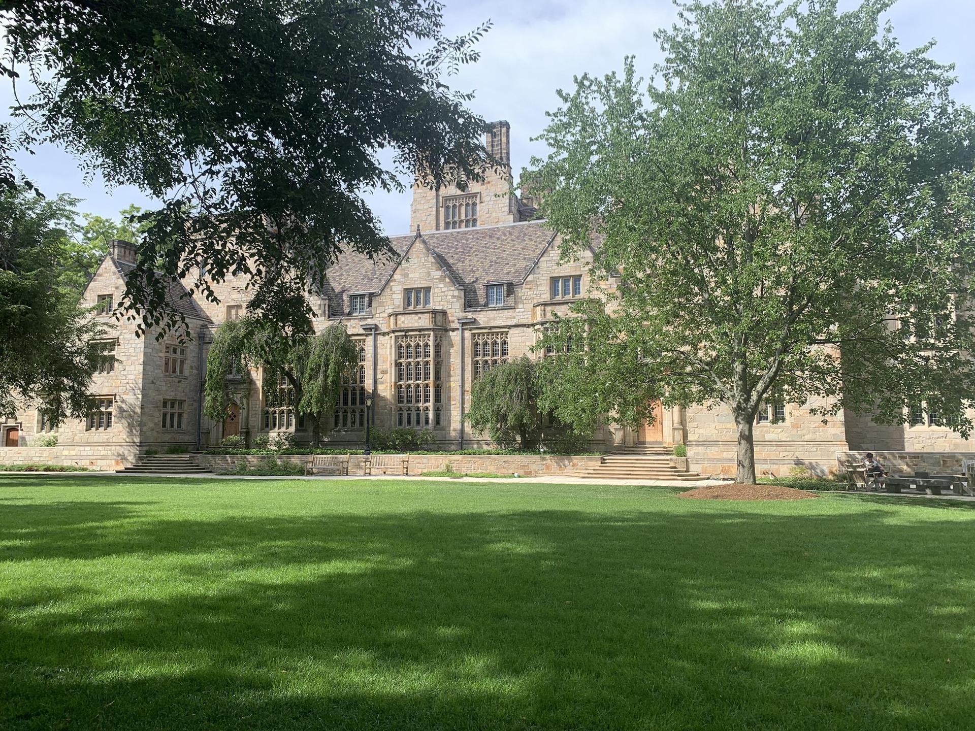 Grand stone building with a large green lawn and mature trees on a bright day.