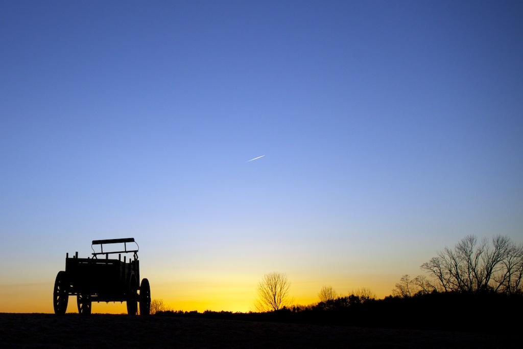 Silhouetted wagon at sunset with a warm glow and blue sky.