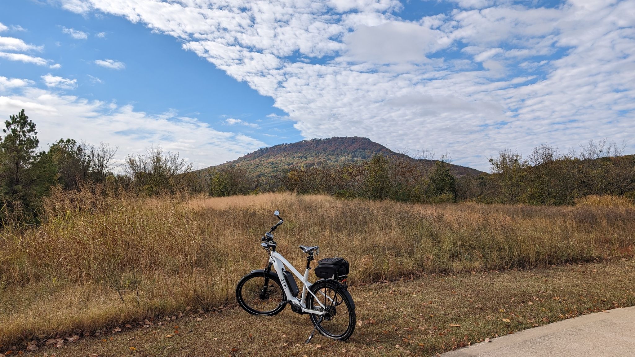 White bicycle on a path, with a grassy field and distant mountain. - View of Lookout Mountain – Blue Goose Hollow Park loop from W. Max Finley Stadium
