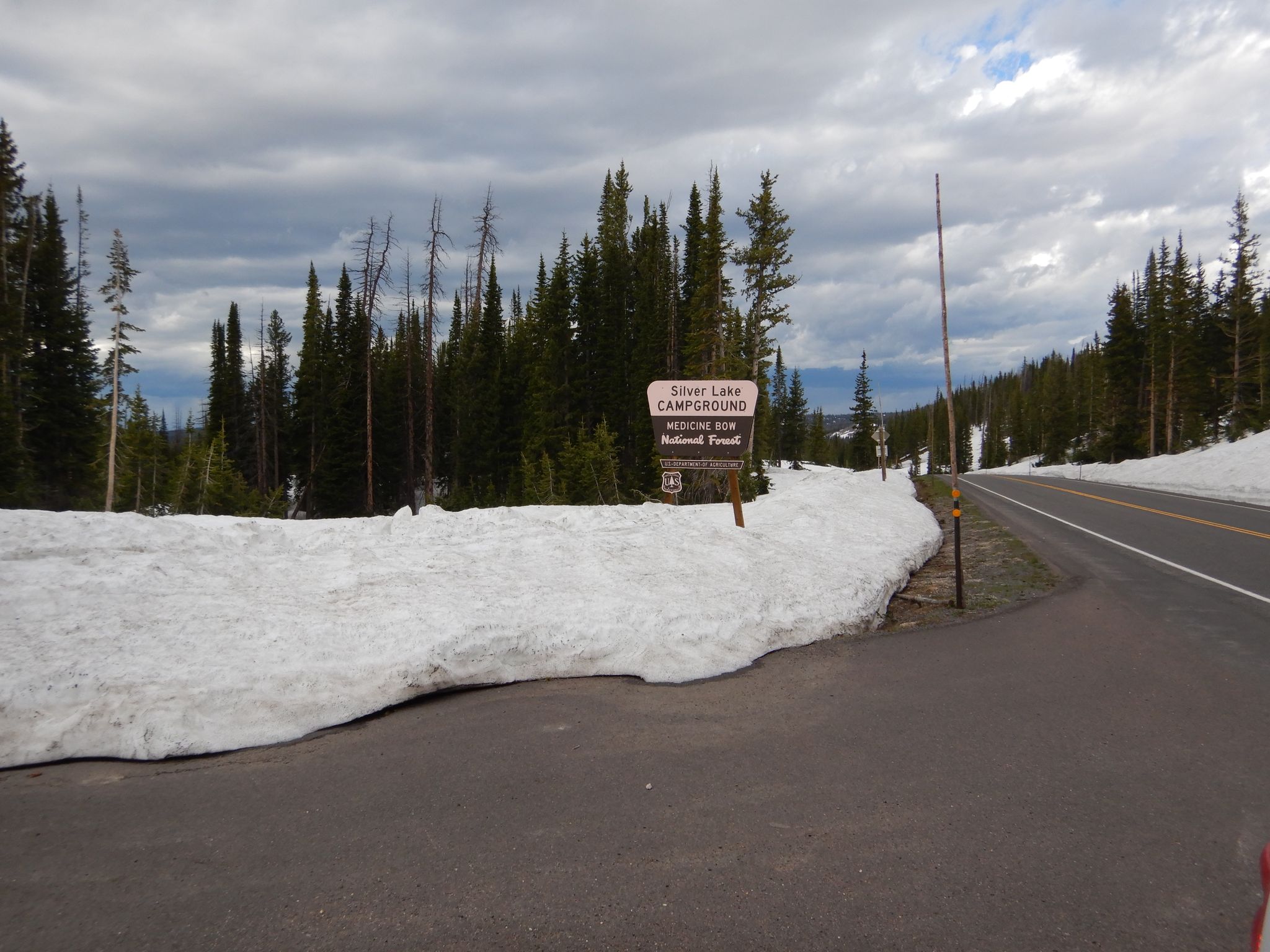 Roadside sign next to a large snowdrift and pine trees. - Silver Lake Trail