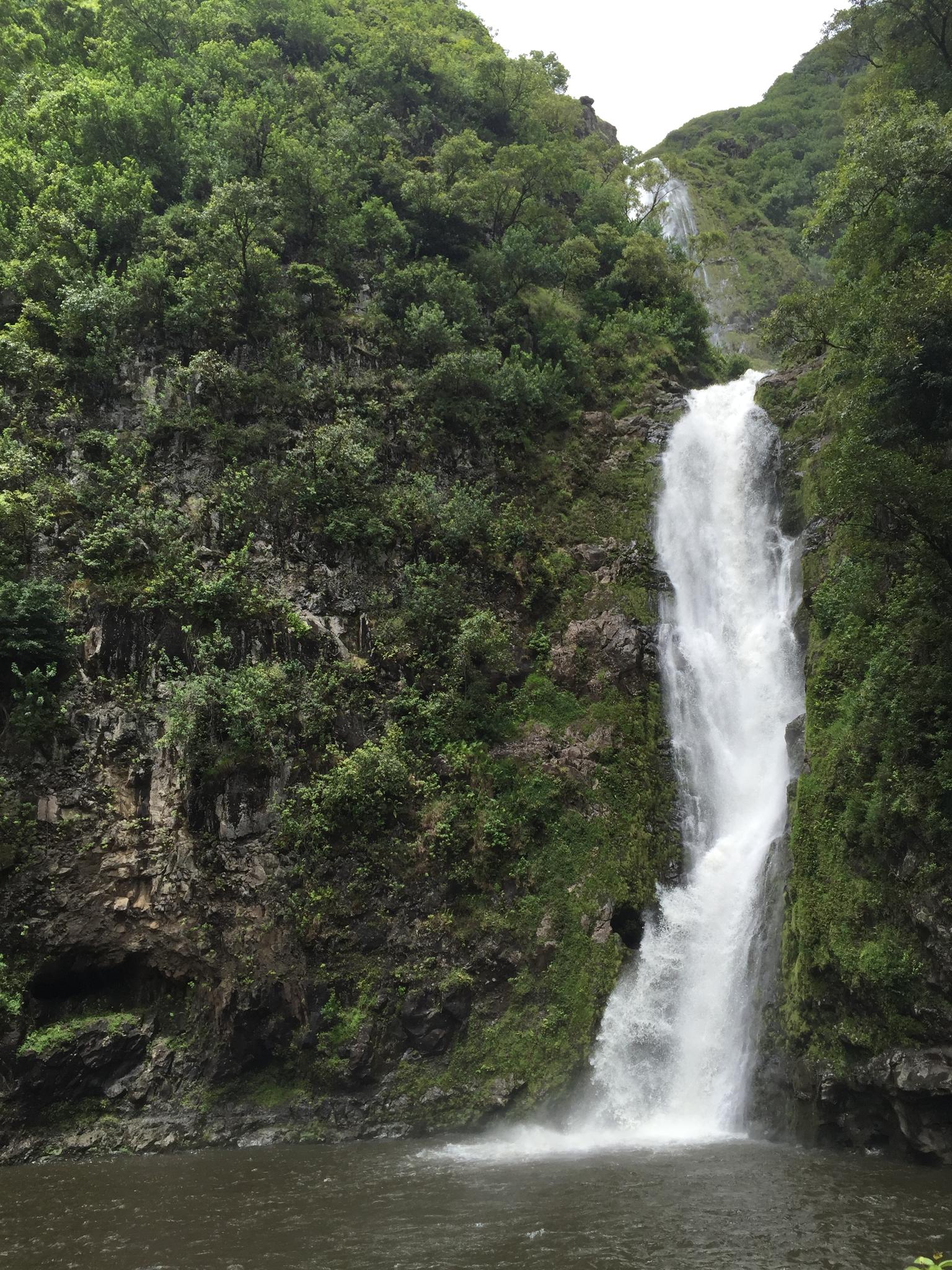 Tall waterfall cascades into a dark pool surrounded by lush green cliffs.