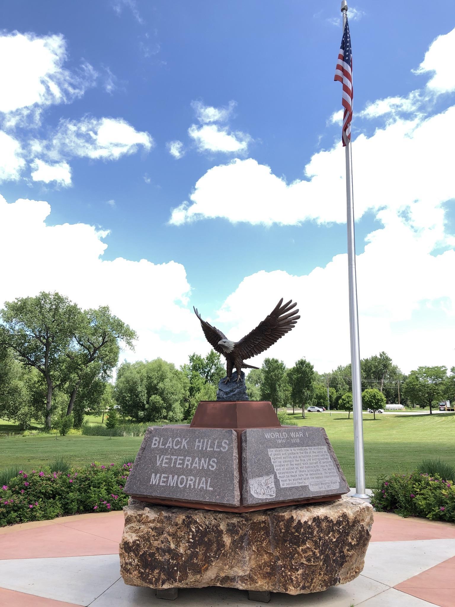 Eagle statue on a veterans memorial with an American flag under a blue sky.