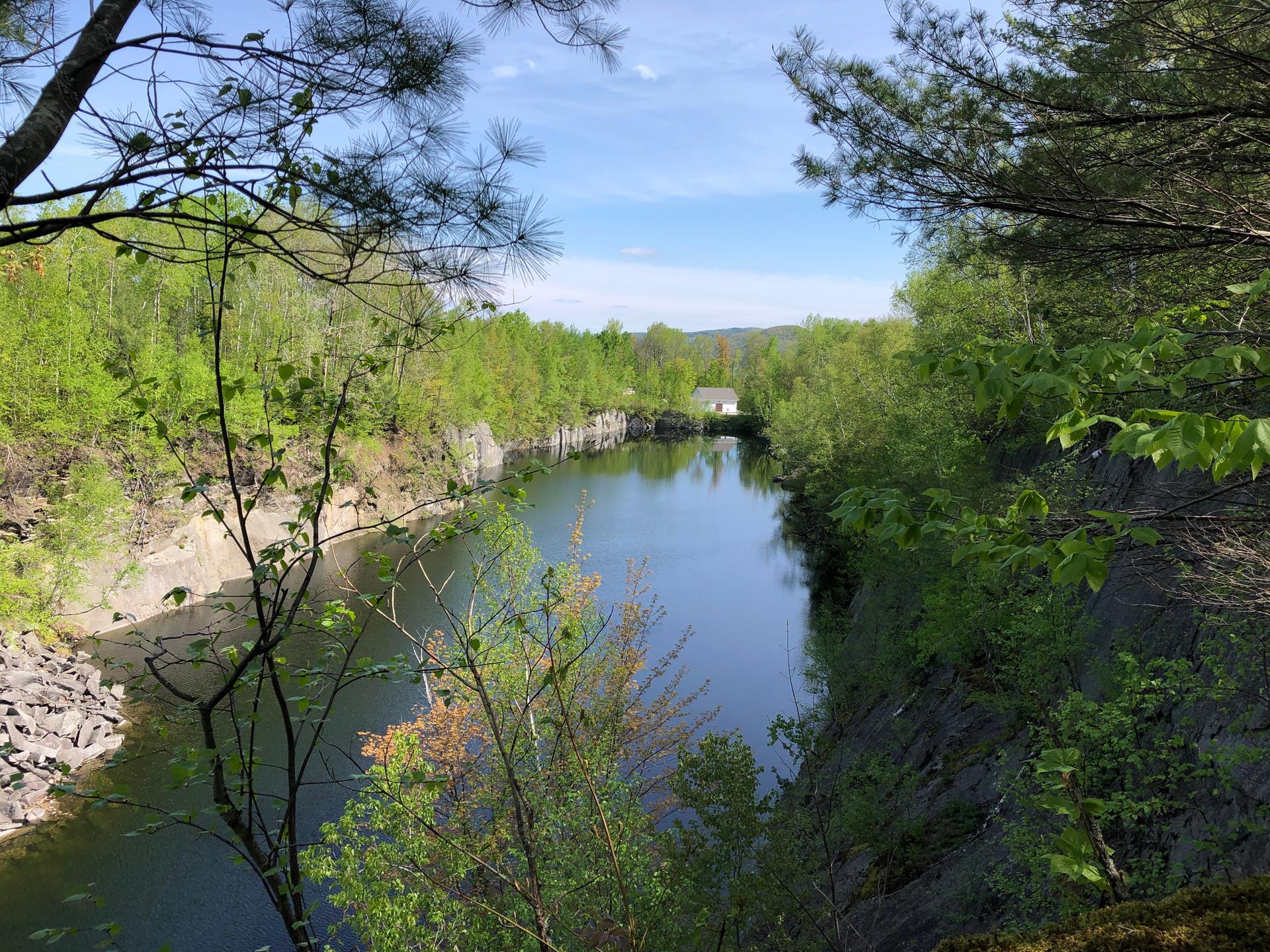 Clear blue lake in a quarry, surrounded by lush green trees under a sunny sky.