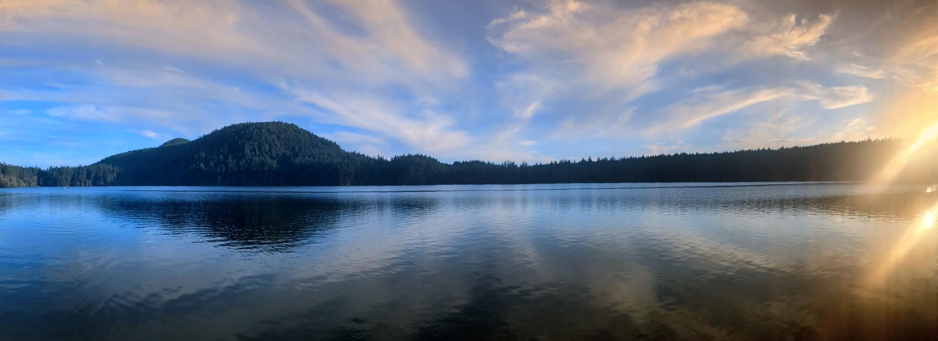 Panoramic view of a calm lake reflecting forested hills under a dramatic sky.