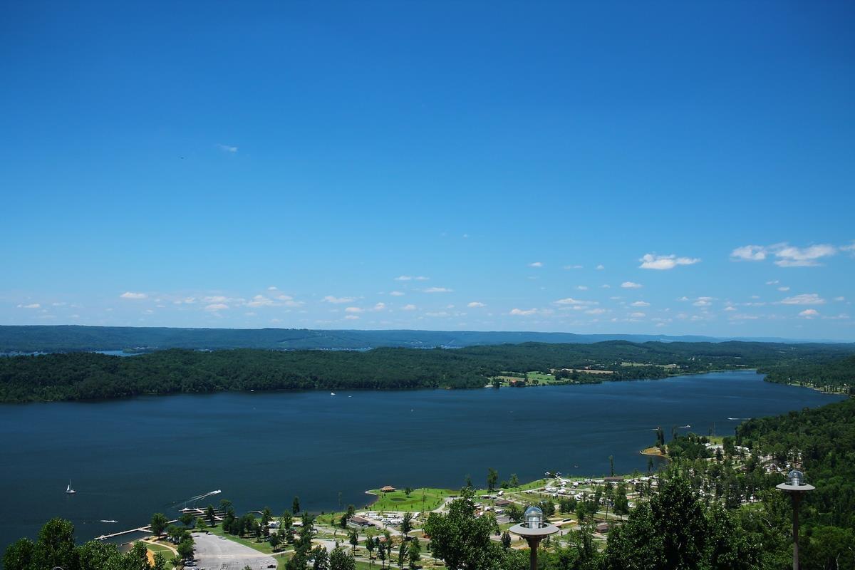 Wide lake surrounded by green hills and boats under a bright blue sky.