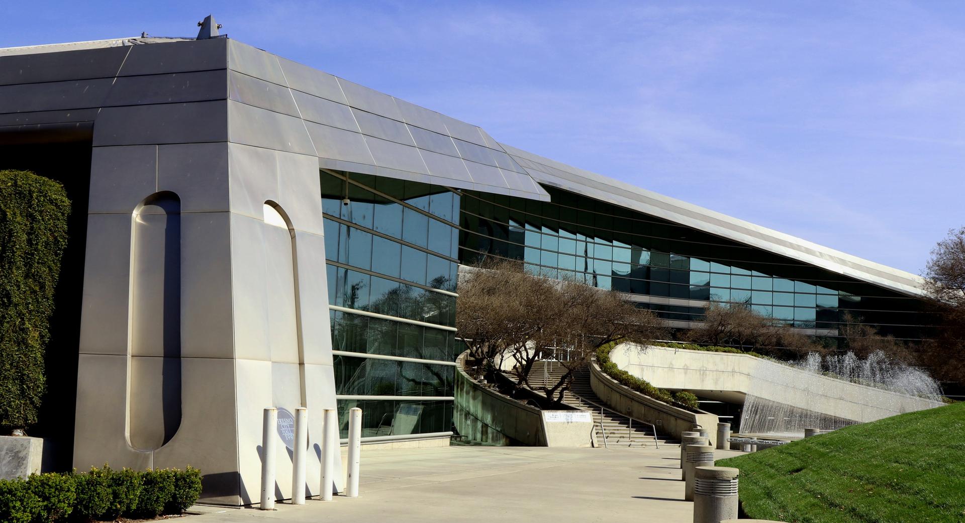 Modern building with glass facade, concrete, and a fountain under sunny skies.