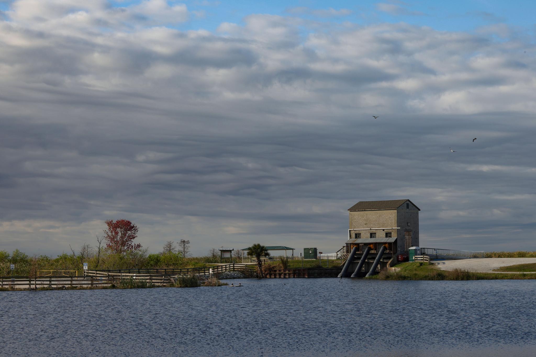 A large body of water with a gray building on stilts under a cloudy sky.