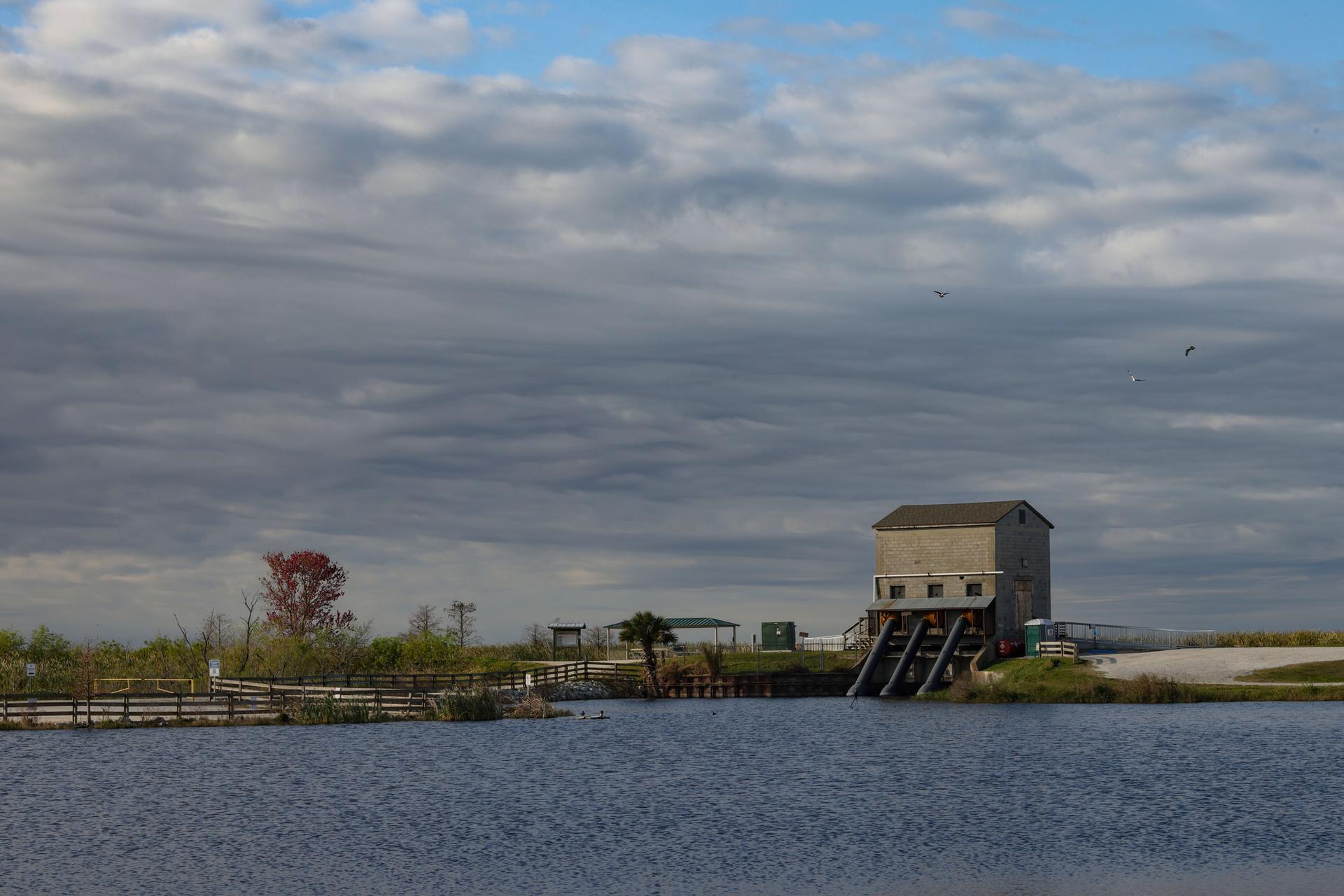 A large body of water with a gray building on stilts under a cloudy sky.