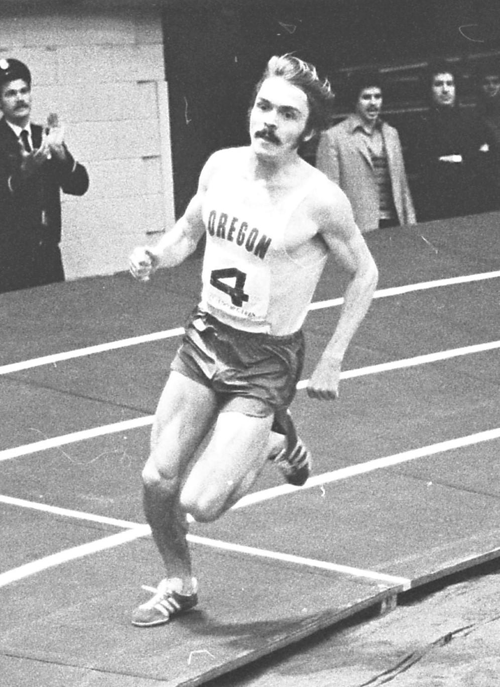 Black and white photo of a male runner on an indoor track.