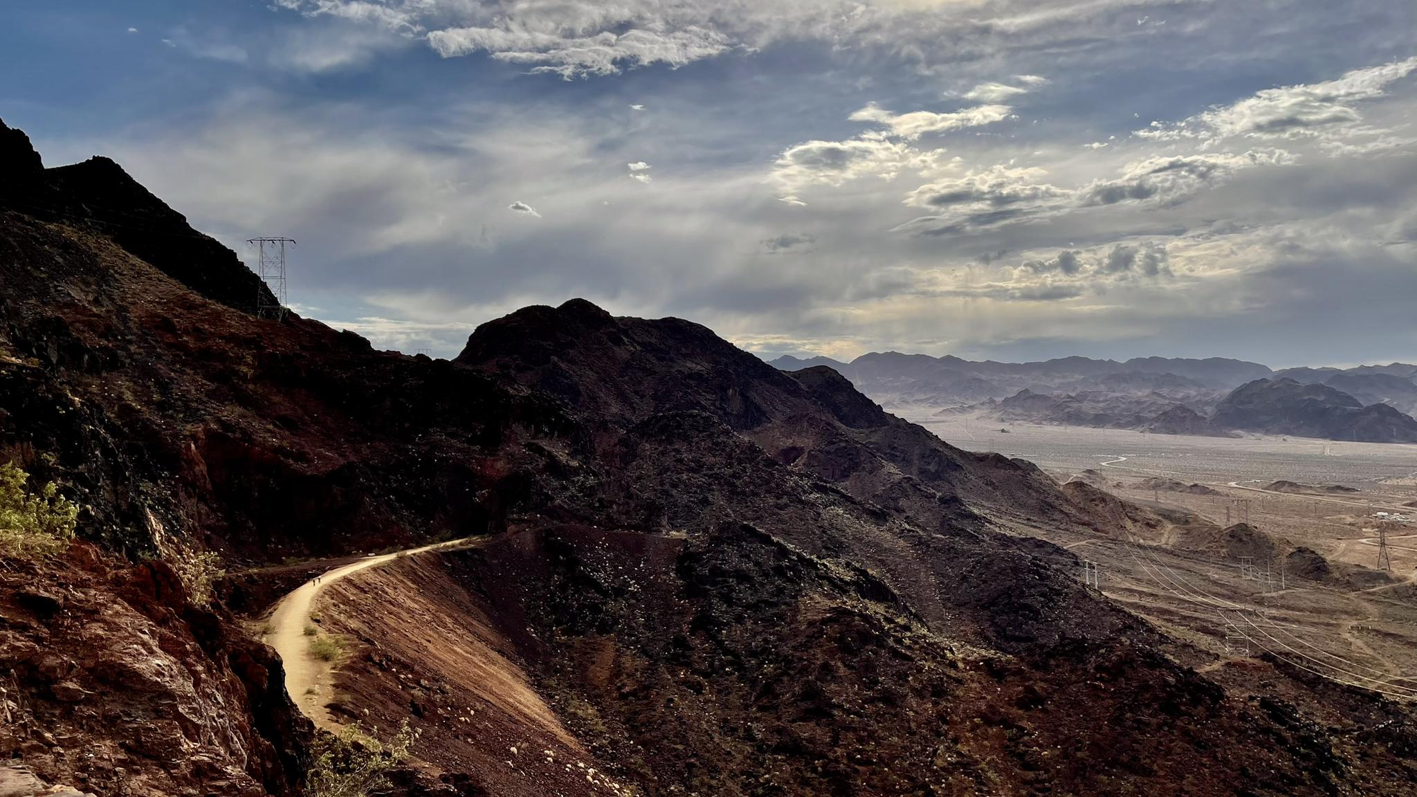 Winding dirt road on a rugged mountain slope under a dramatic cloudy sky.