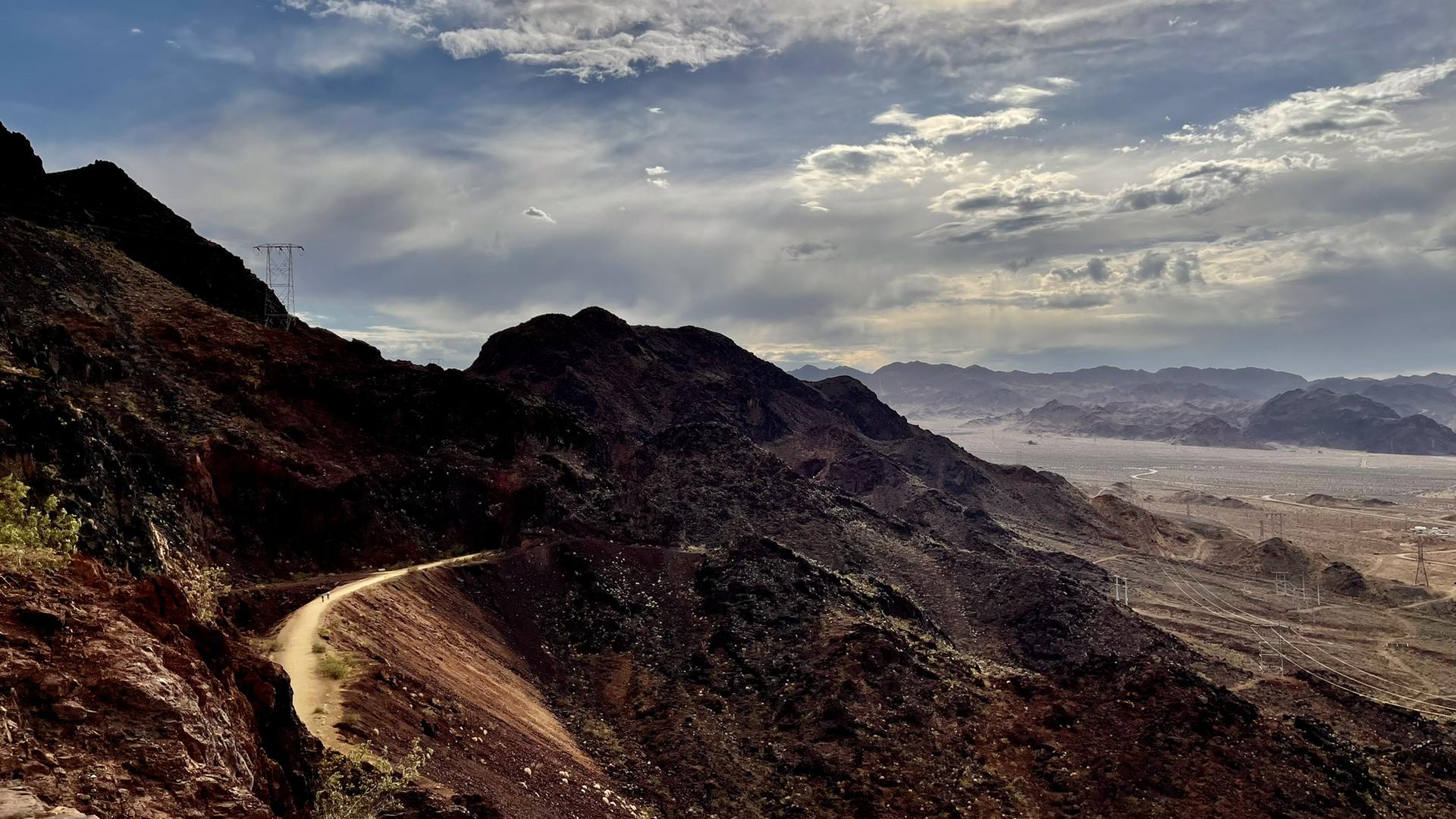 Winding dirt road on a rugged mountain slope under a dramatic cloudy sky.