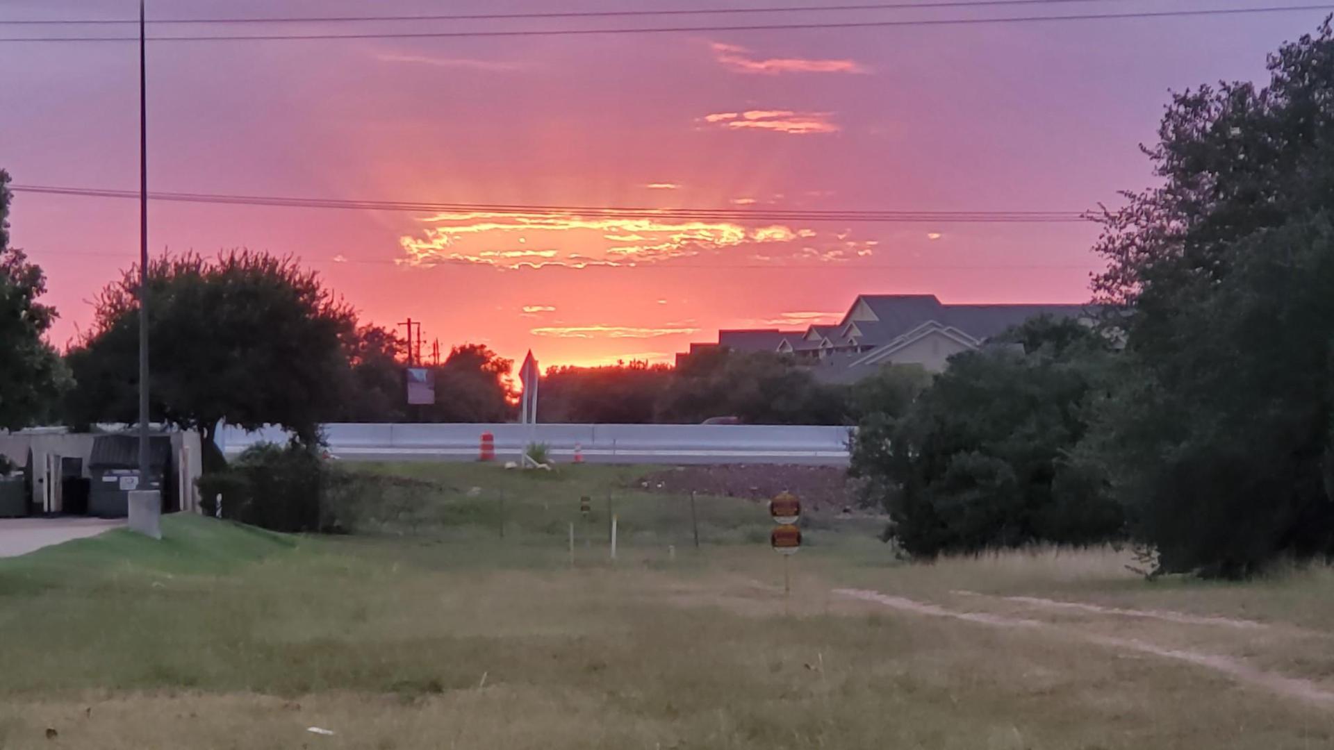 Dramatic pink and orange sunset over a landscape with buildings and trees.