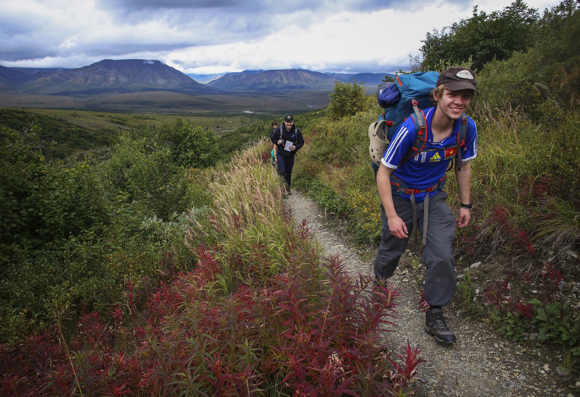 Two backpackers hiking on a narrow trail through colorful foliage.