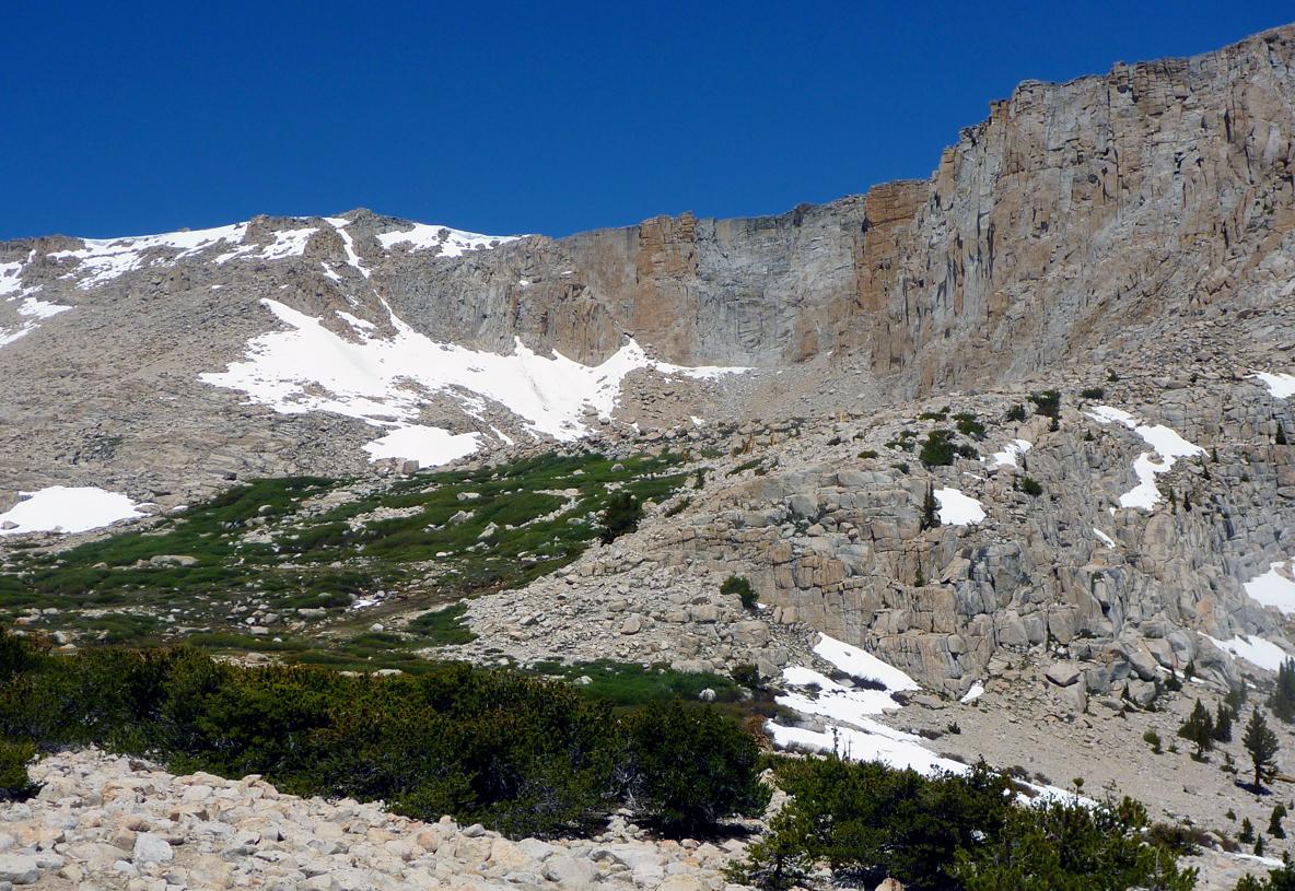 Vast rocky mountains with snow patches and green vegetation under a clear blue sky.