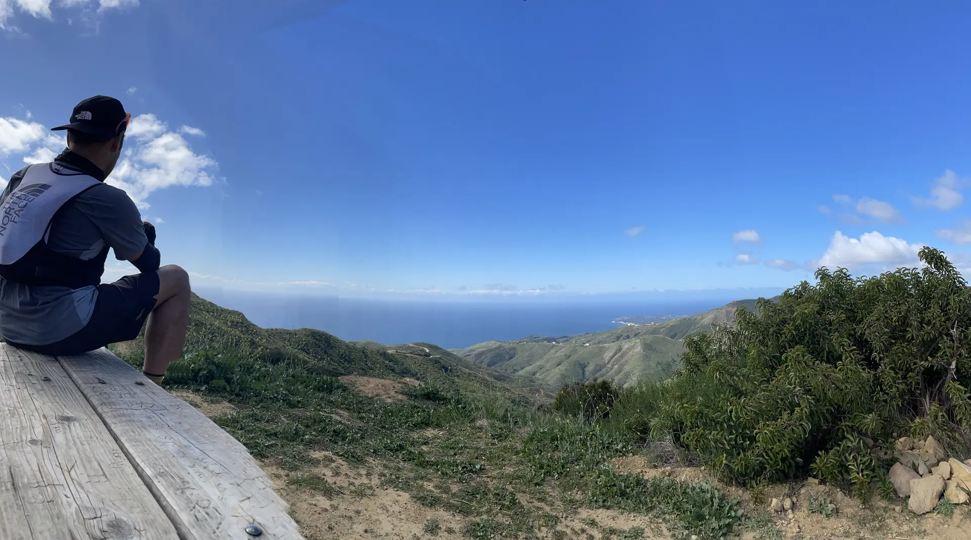 Person sitting on a bench, admiring the vast ocean and hilly landscape.
