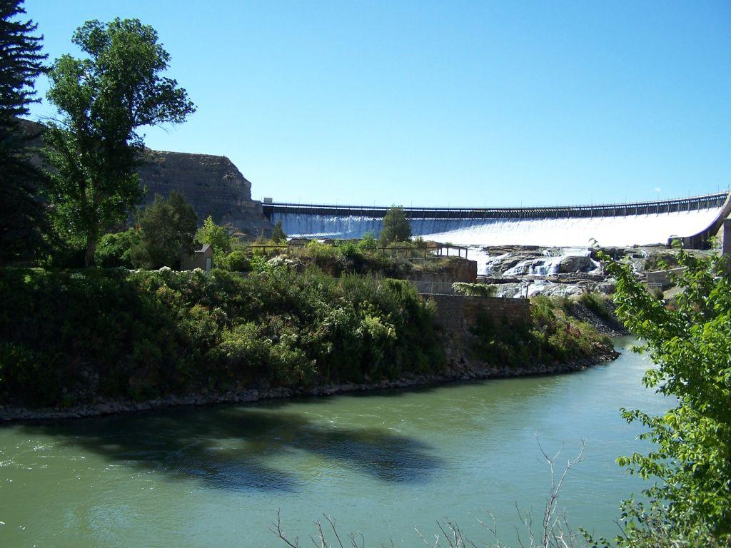 Wide dam with water flowing into a river on a sunny day.