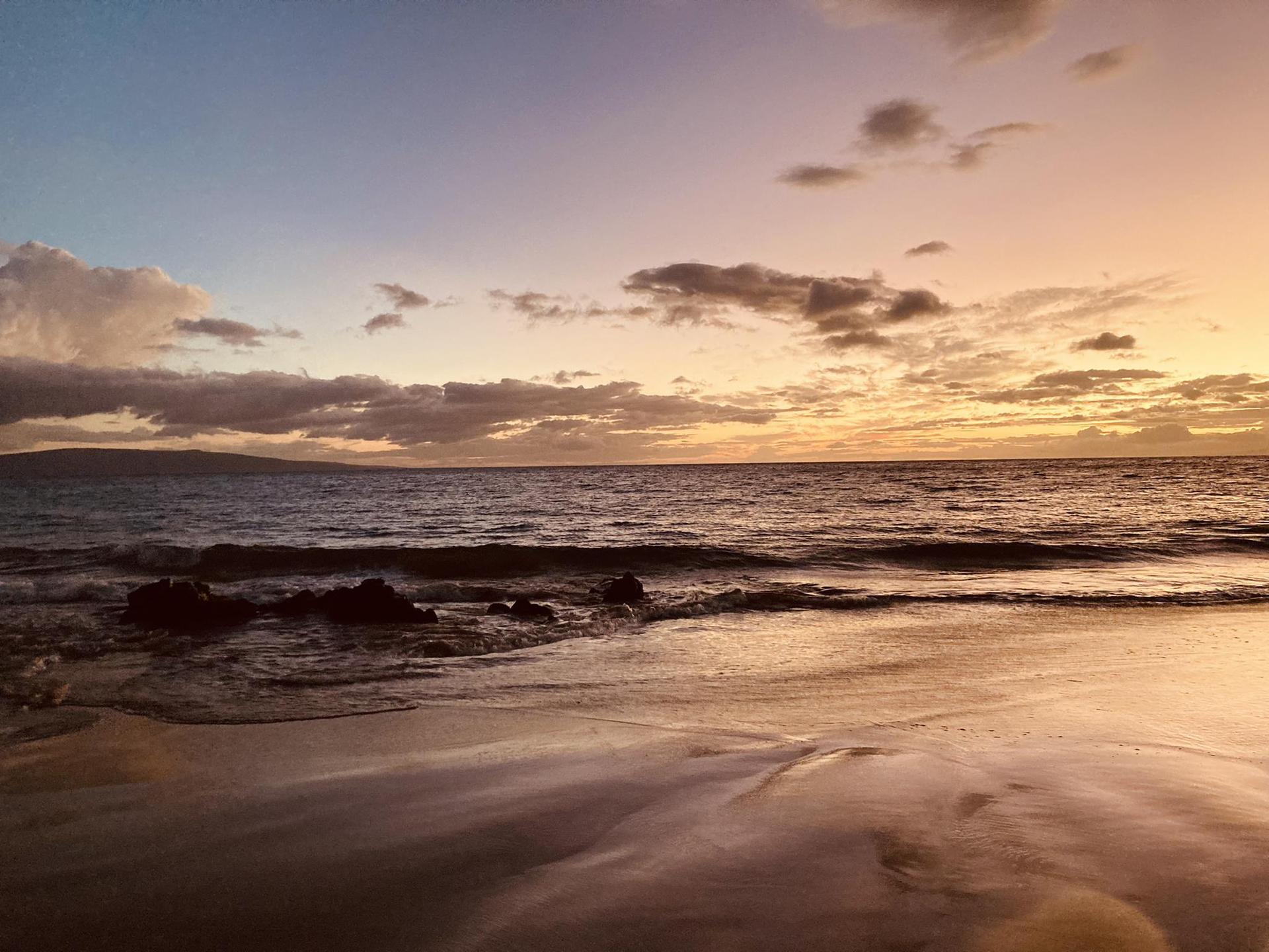 Sunset over ocean waves, with soft orange and purple hues in the sky.