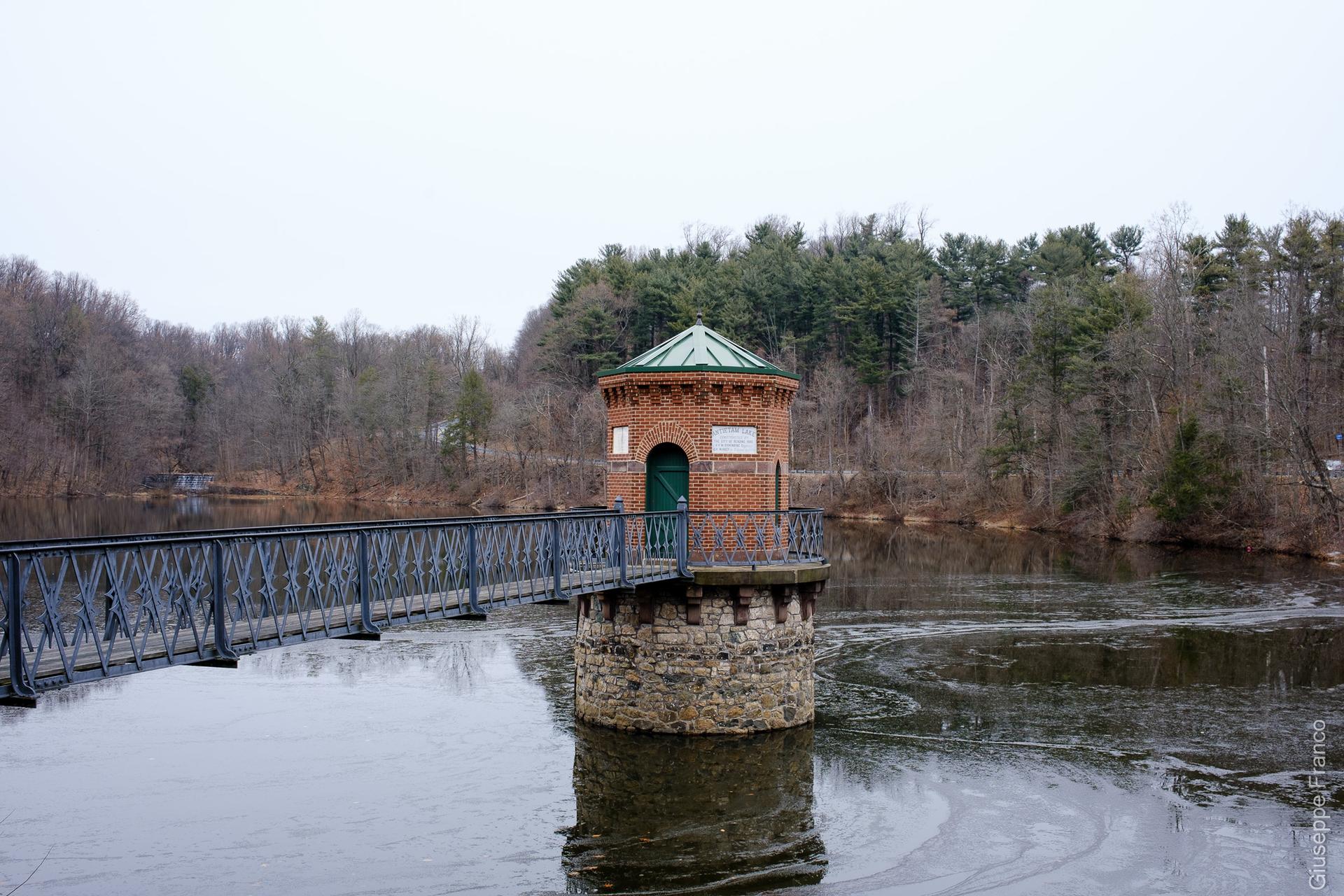 A brick tower with a green roof and bridge over a partially frozen lake.