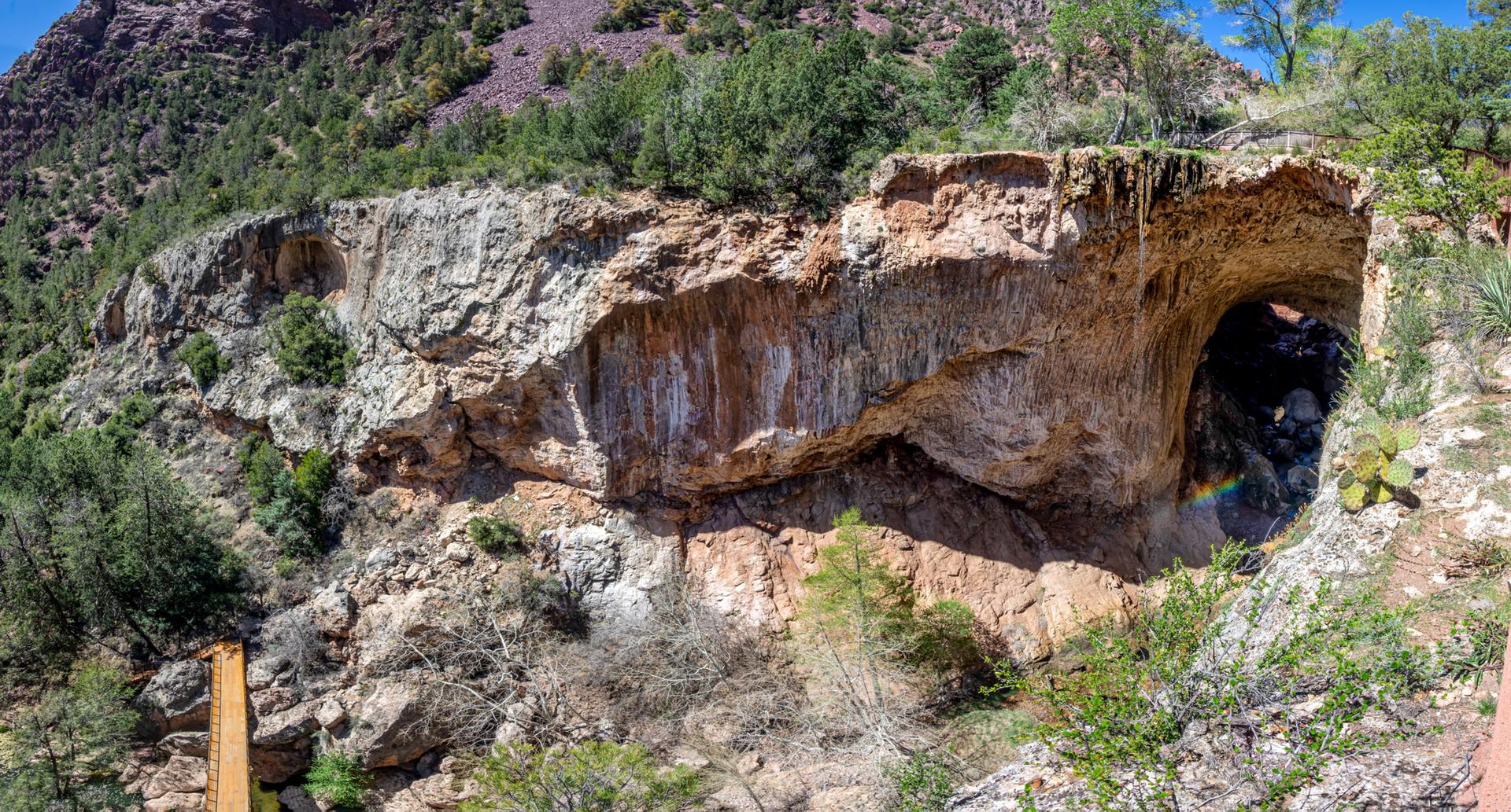 Large natural rock arch and cave in a sunny, rugged, green landscape.