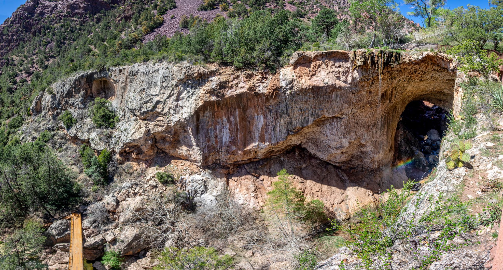 Large natural rock arch and cave in a sunny, rugged, green landscape. - Gowan, Pine Creek, and Anna Mae Trail Loop