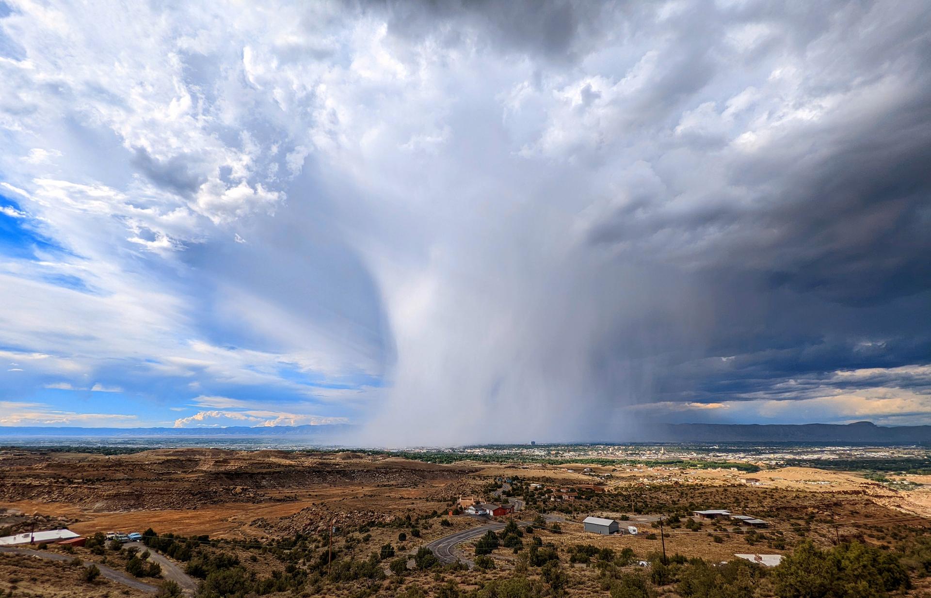 A massive rain shaft descends over a wide desert landscape.