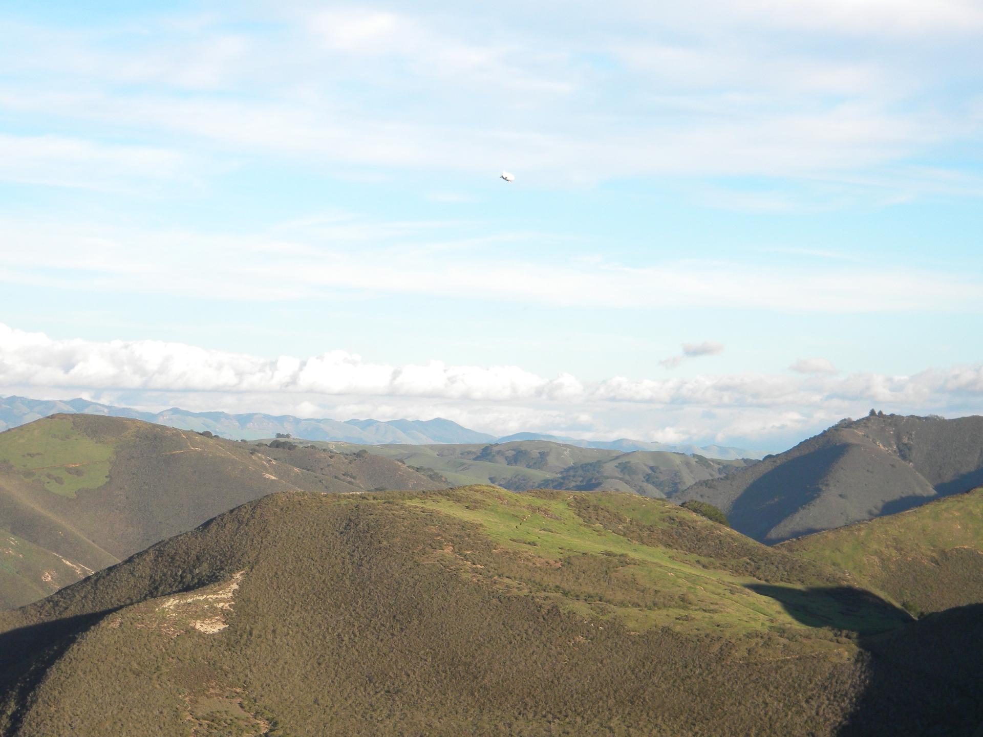 Expansive view of rolling green hills under a partly cloudy sky.