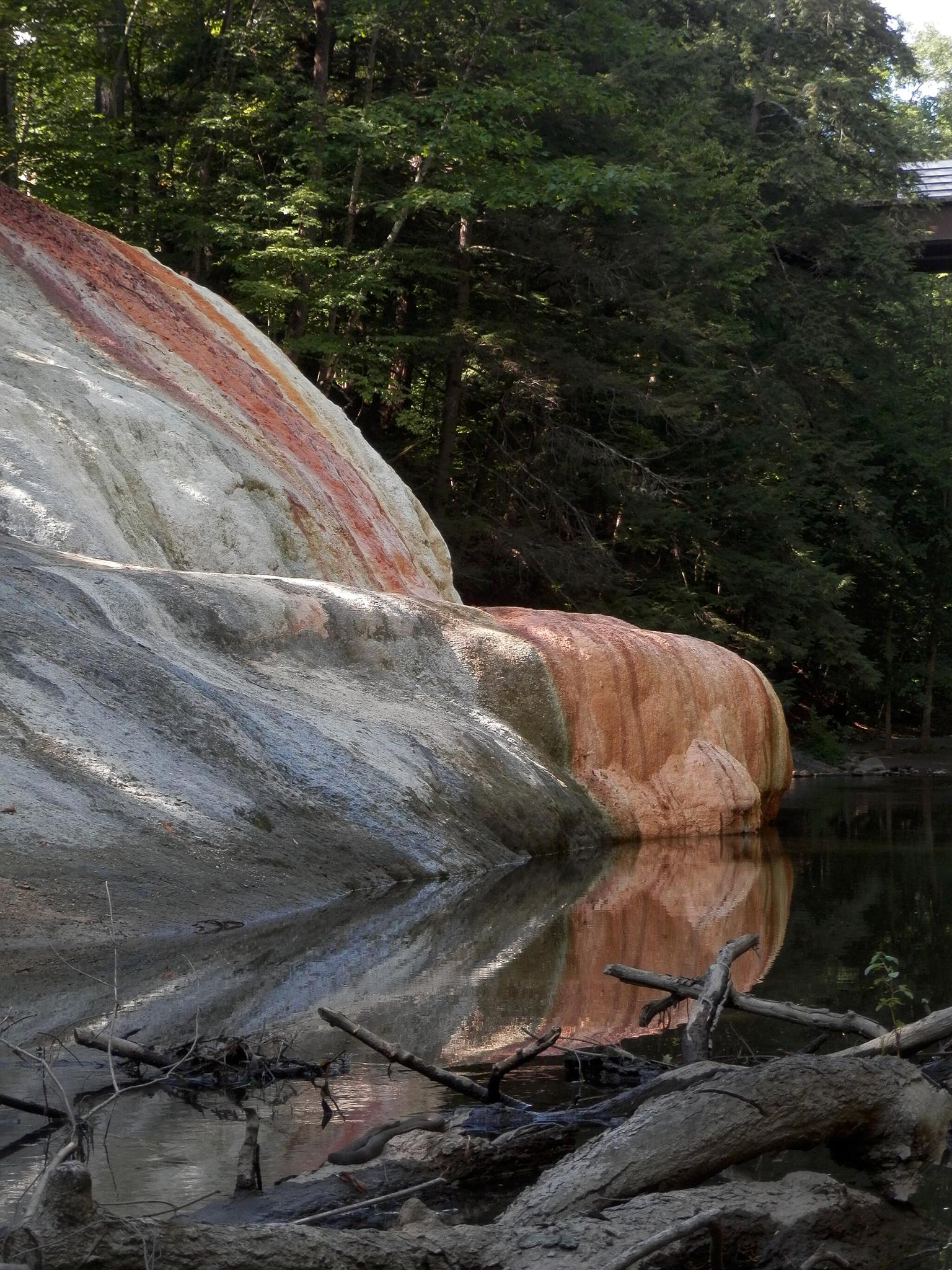 Colorful mineral deposits on a rock face reflecting in calm water.