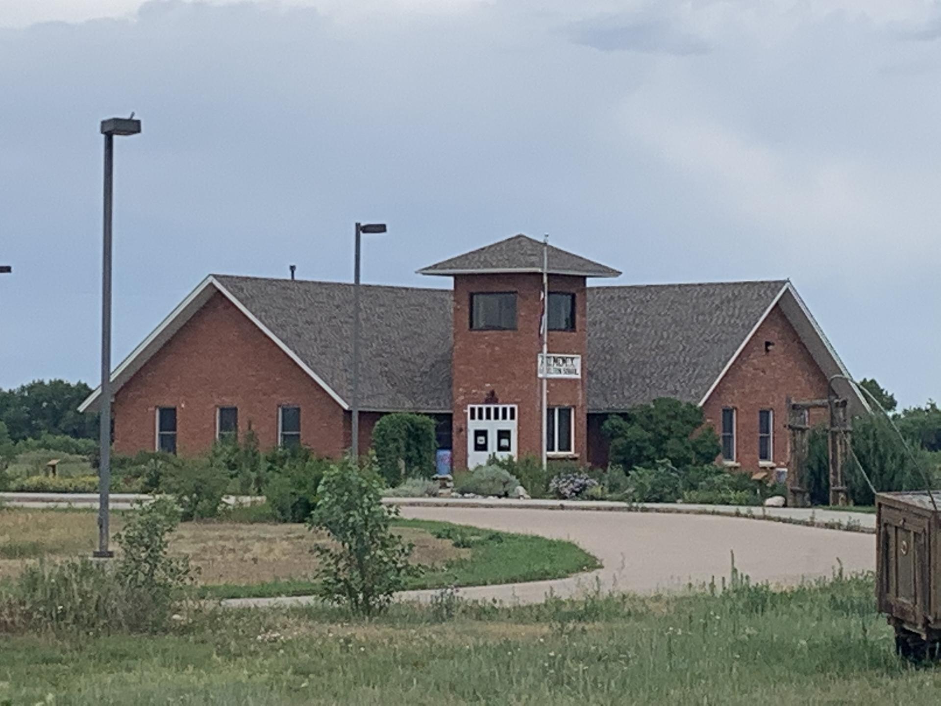A large brick building with a central tower, surrounded by green grass under an overcast sky.