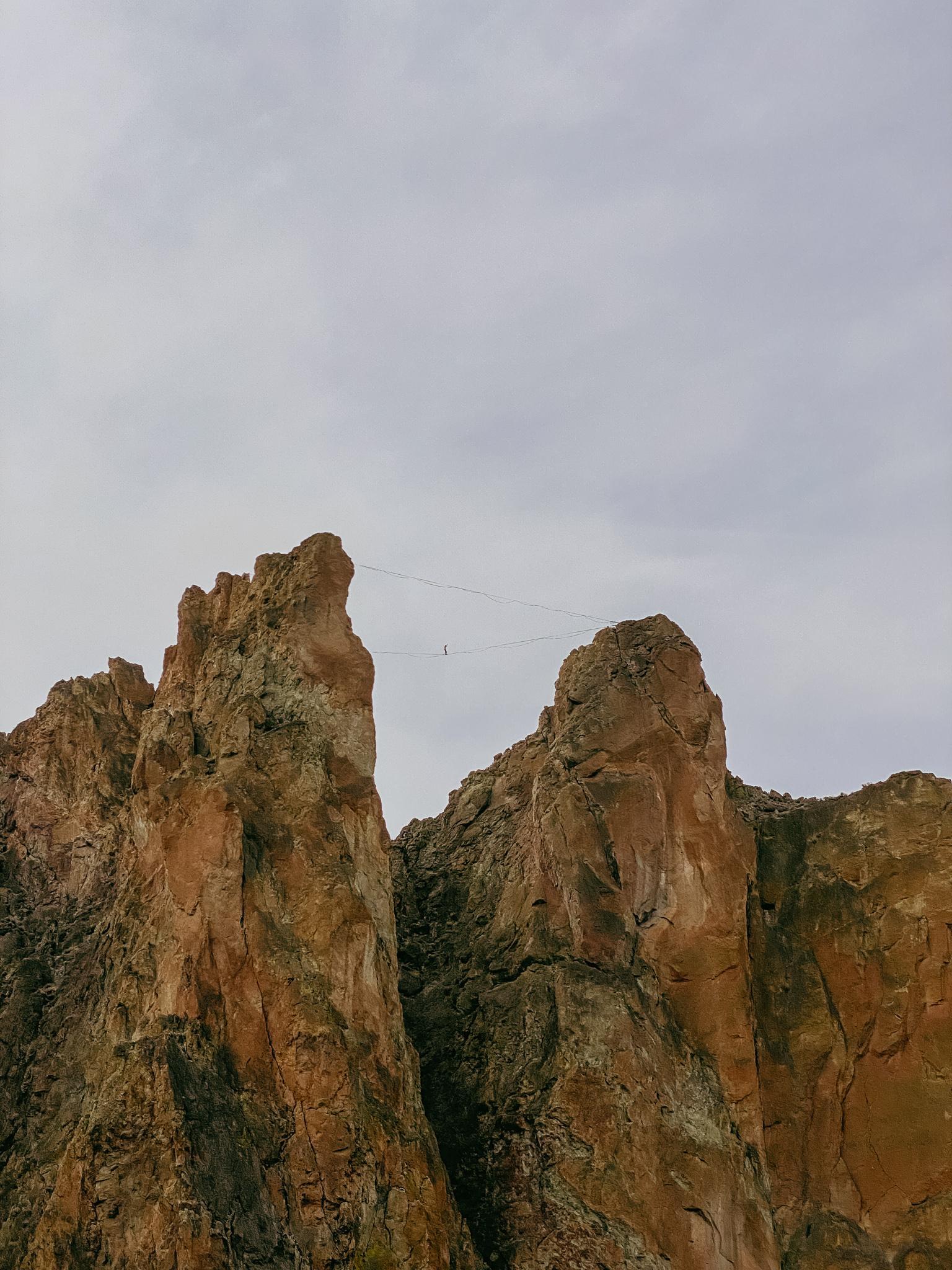 Two rugged rock spires with a slackline stretched between them under an overcast sky.
