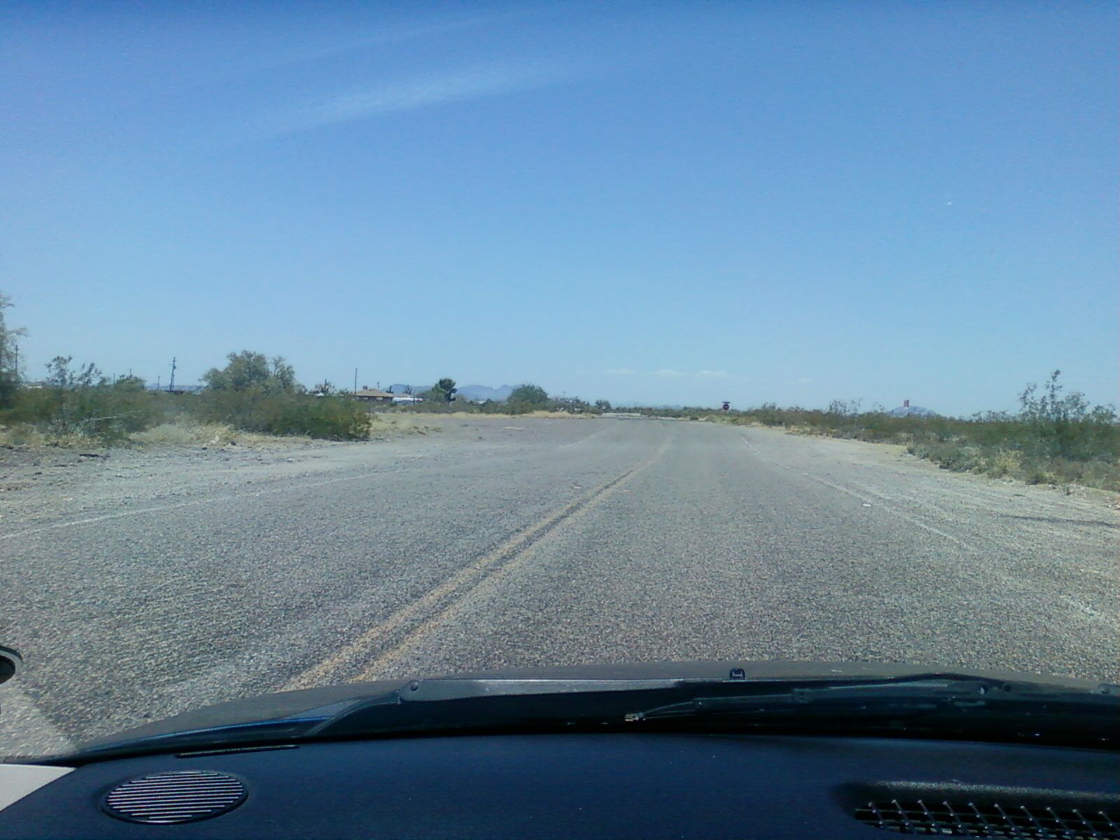 Desert road stretches ahead from car's view under a bright blue sky. - The Road To Nowhere (Sun Valley Parkway)